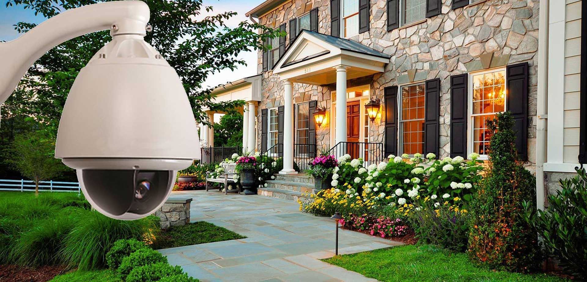 Security camera overlooking a well-manicured yard and a stone house with shutters.