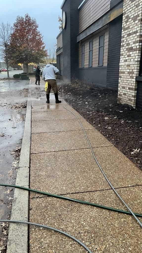 A man is cleaning a sidewalk in front of a building with a hose.