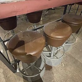 A row of brown bar stools are sitting under a glass table.