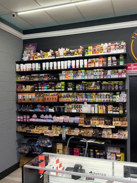 Shelves stocked with vape products in a store. Dark wall, black shelves, and a glass display case in front.