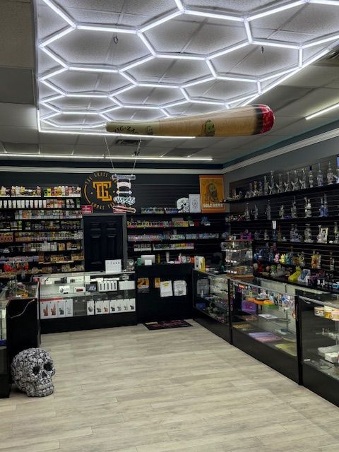 Interior of a smoke shop with display cases, a large joint prop, and honeycomb-patterned ceiling lights.