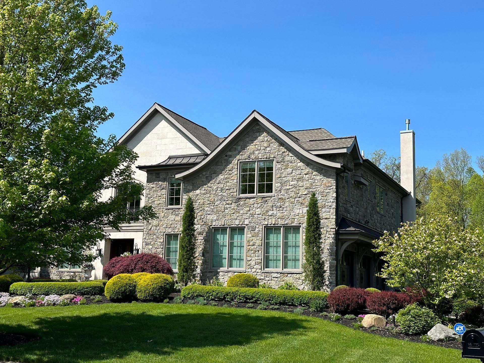 Stone house with green shutters and a manicured lawn under a clear blue sky