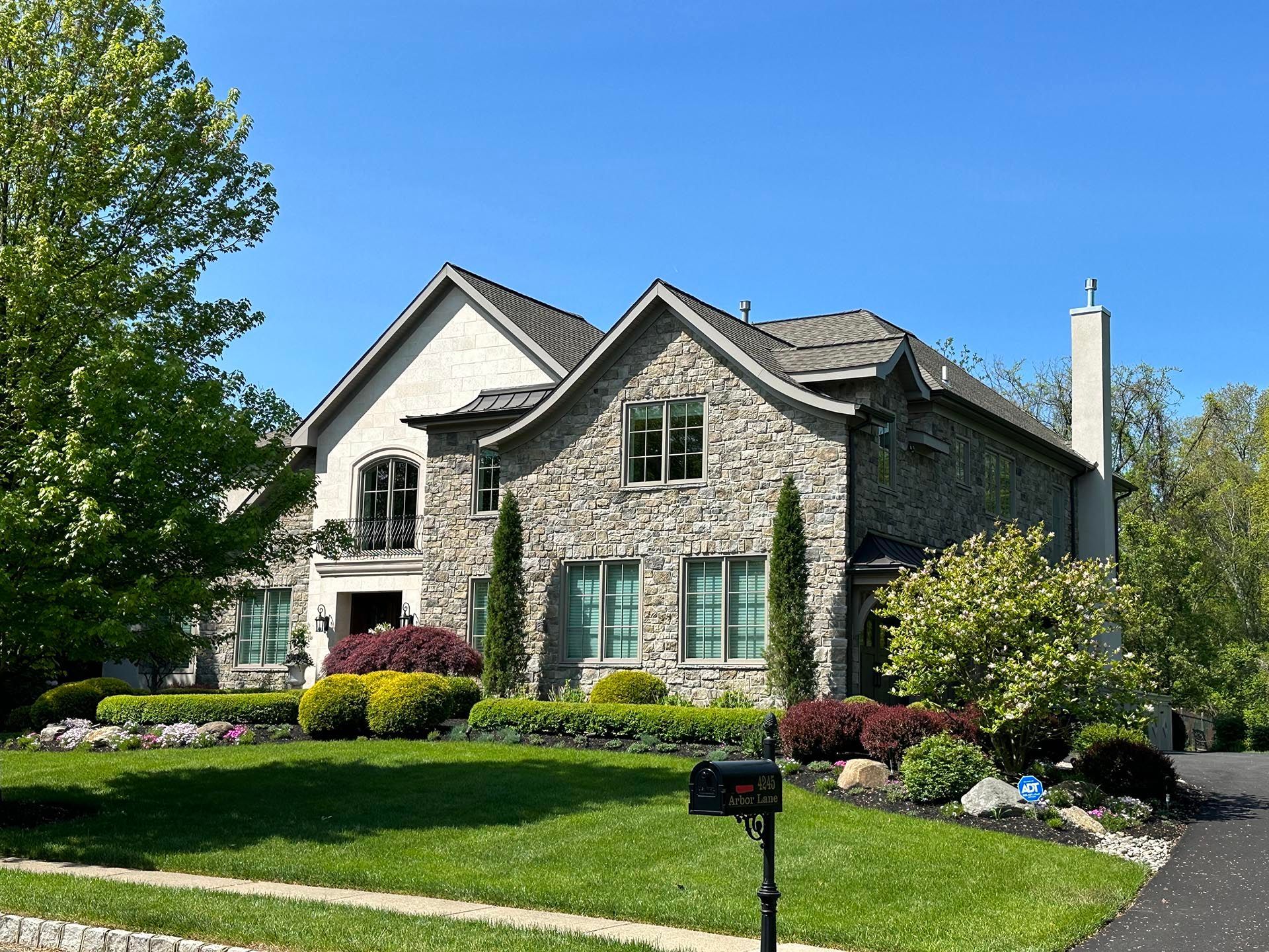 Stone house with green shutters and manicured lawn under a clear blue sky