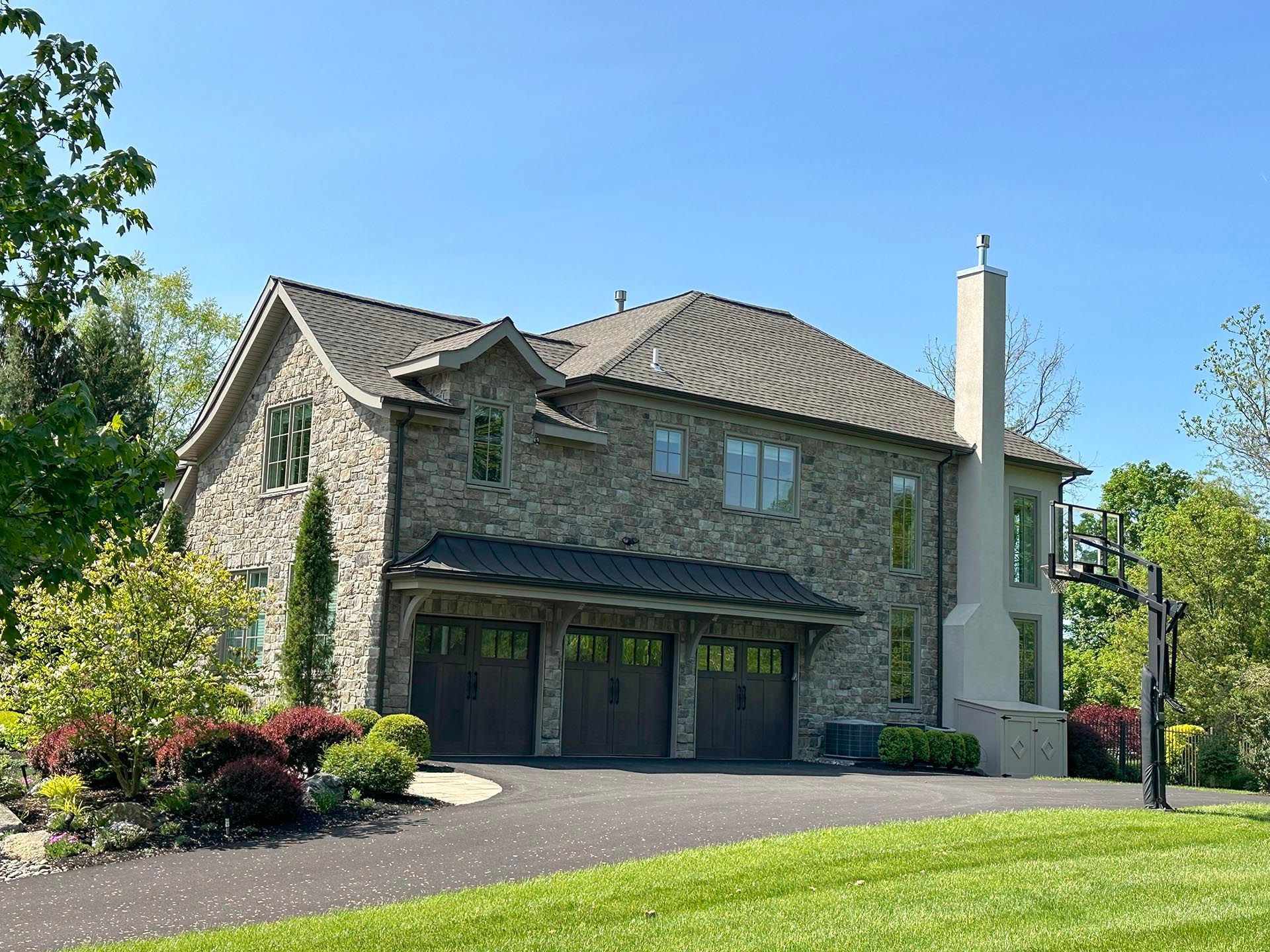 Stone house with a tiled roof, garage doors, and landscaped front yard on a sunny day