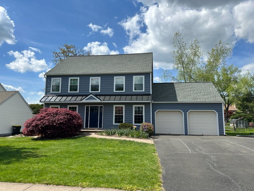 Two-story gray house with attached double garage, driveway, and well-kept lawn under a partly cloudy sky