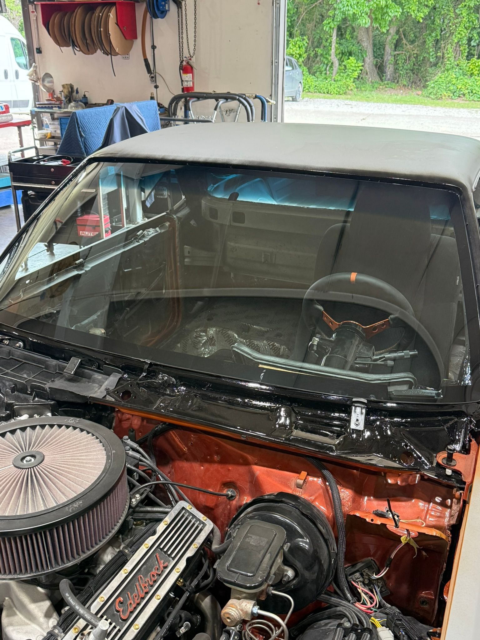 Red vintage car under repair in a garage, with exposed engine and windshield removed.
