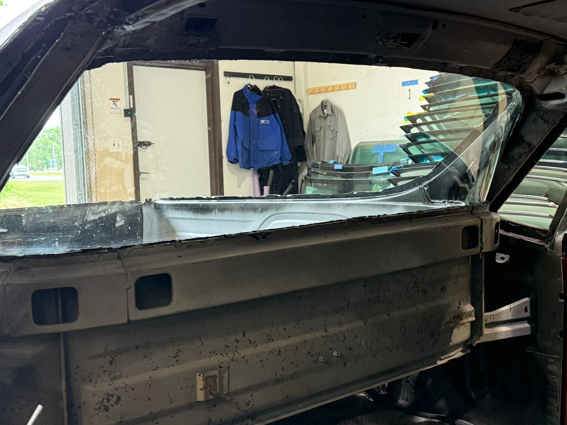 Interior of a stripped car body in a garage, with jackets hanging on the wall in the background.