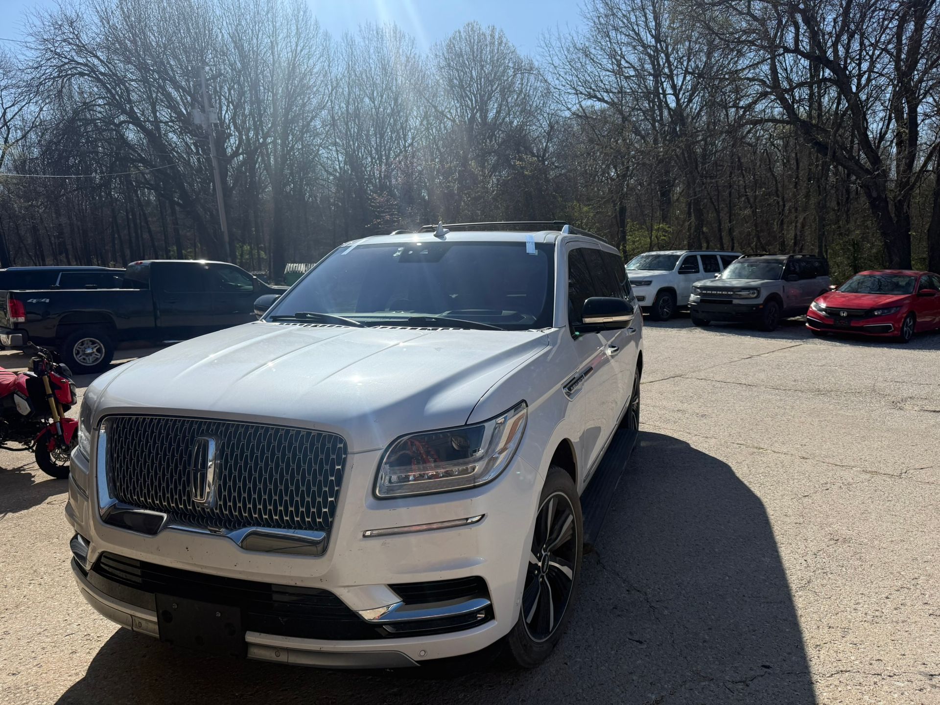 White luxury SUV parked in a lot on a sunny day with trees in the background