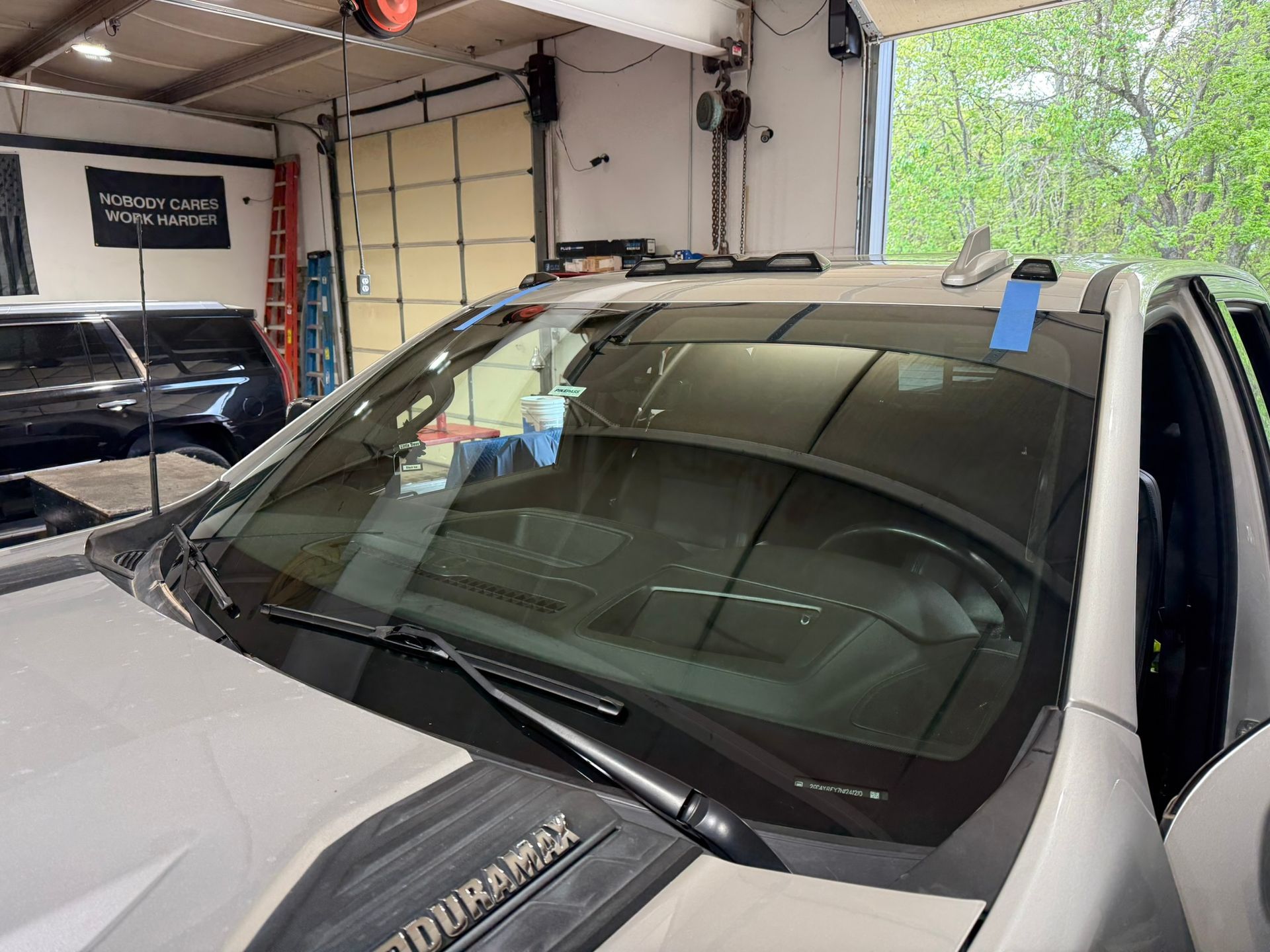 White SUV in a garage with a cracked windshield being taped for repair