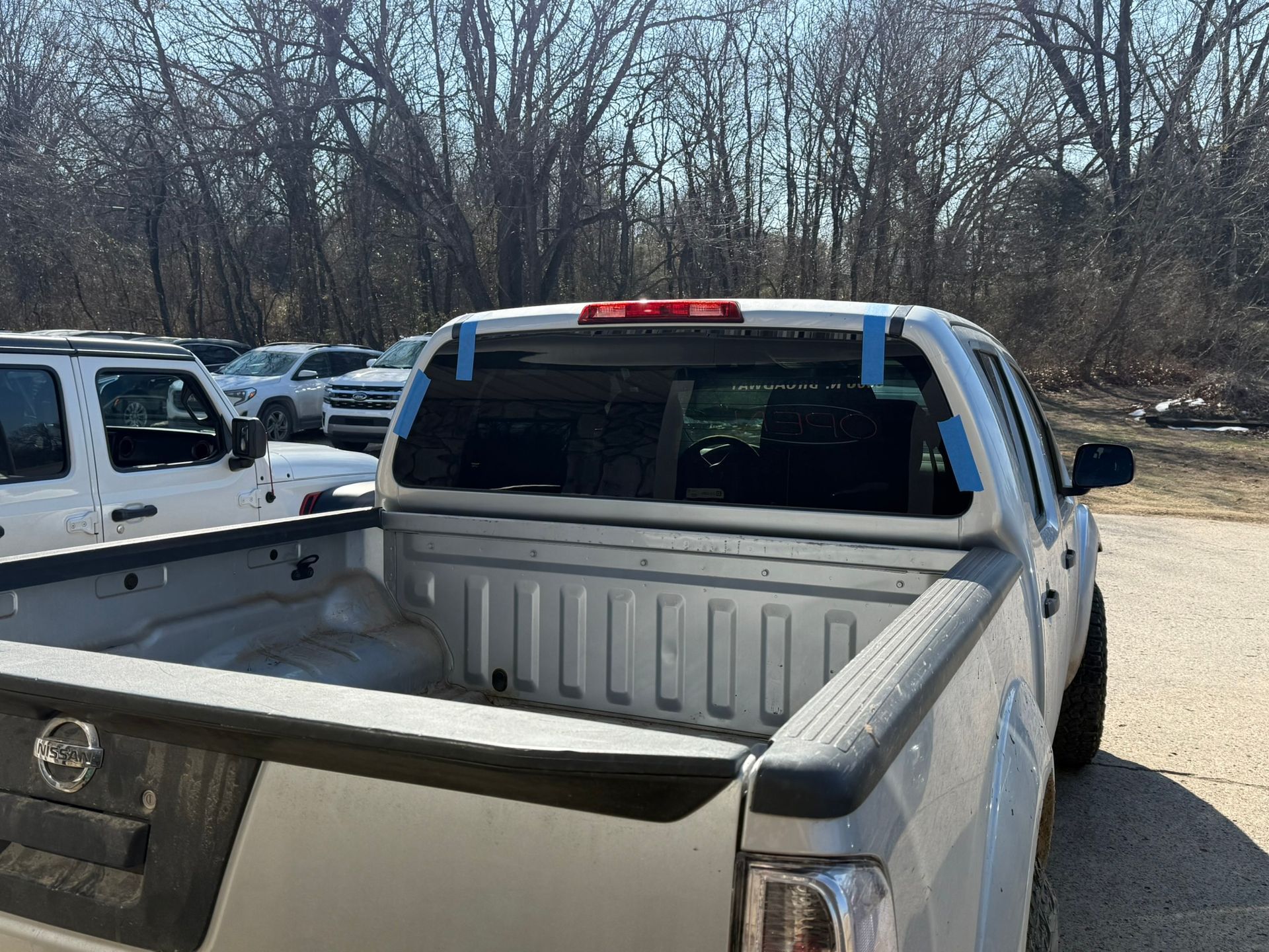 White pickup truck with blue tape on rear window; parked outdoors.