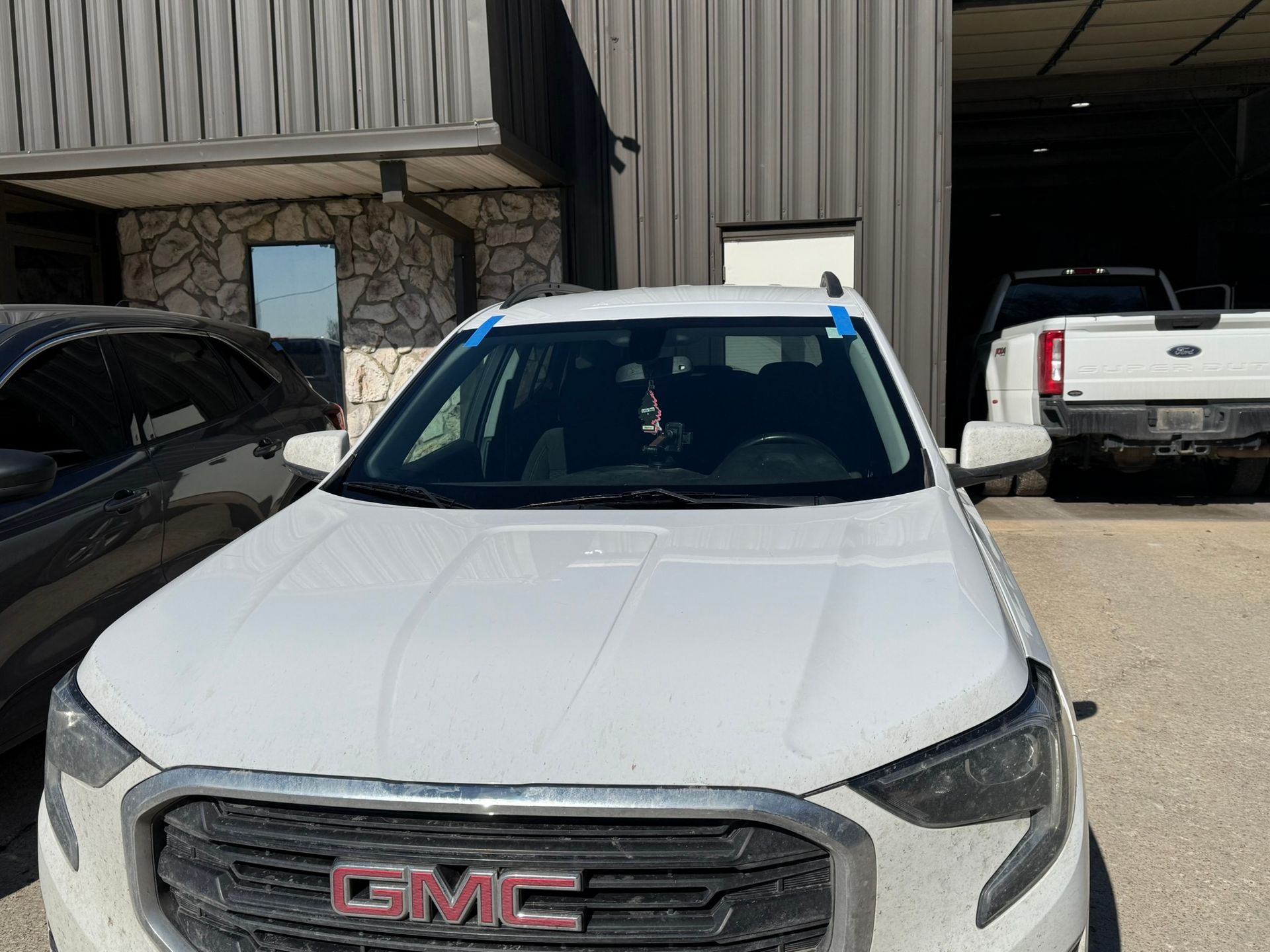 White GMC SUV with blue tape on the windshield in front of a building with stone and metal siding.