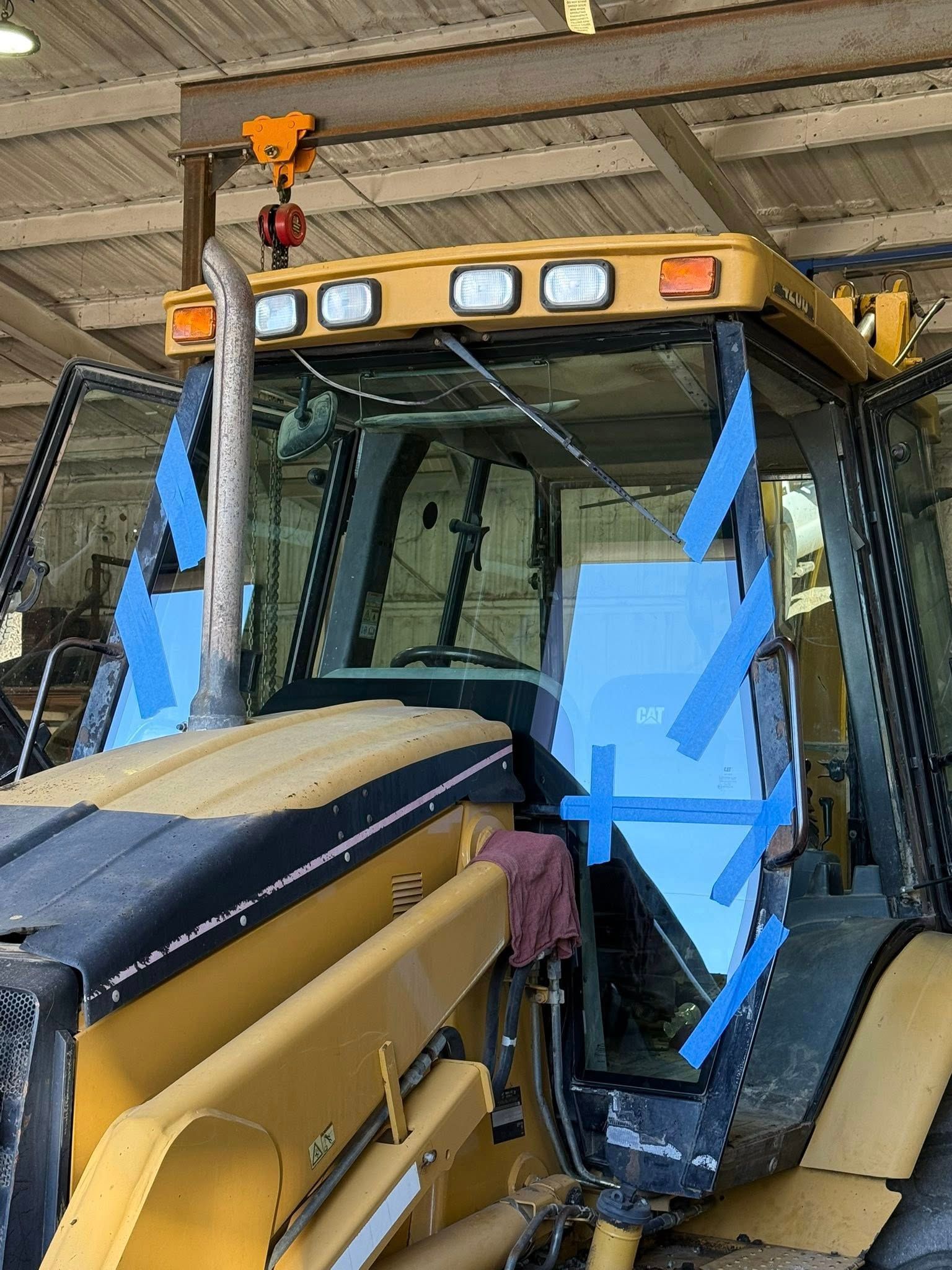 Yellow construction vehicle with taped-up windows, inside a workshop.