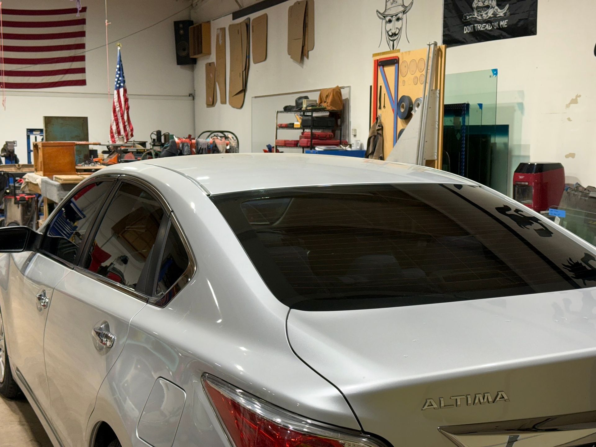 White sedan in a garage workshop, with tools, an American flag, and shelves in the background.