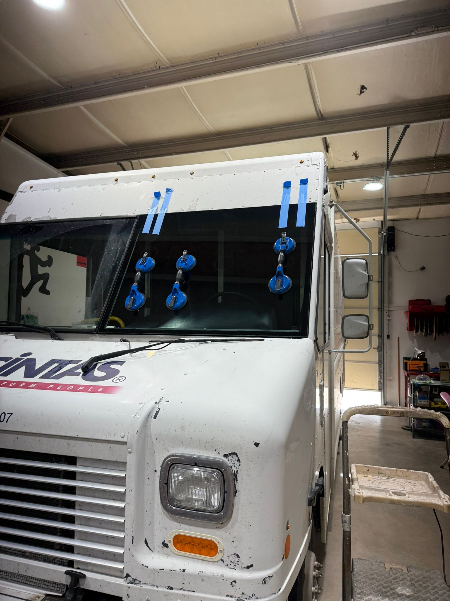 White truck windshield with suction cups, blue tape; inside a garage.