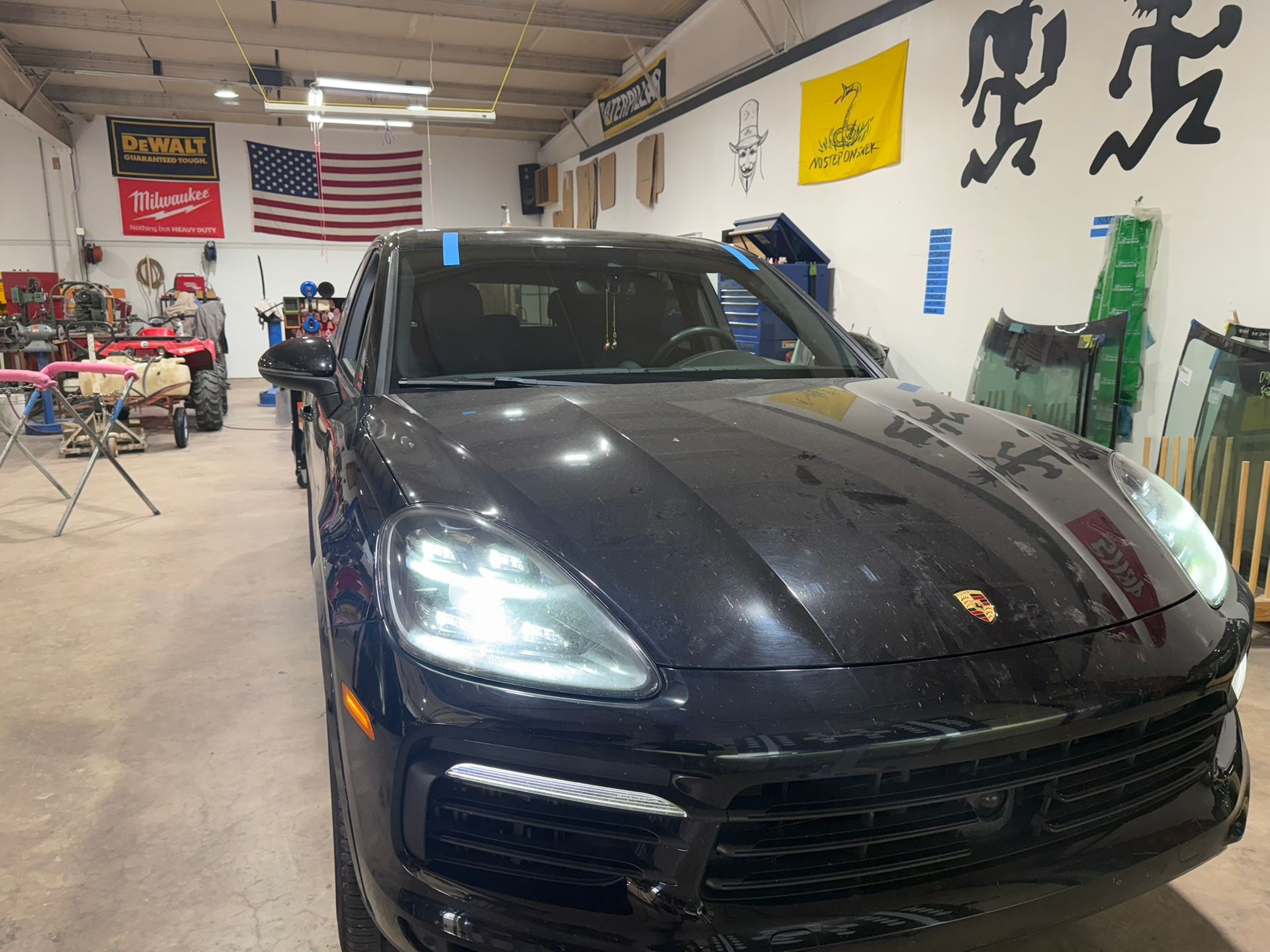 Black Porsche SUV inside a garage with tools, American flag, and yellow