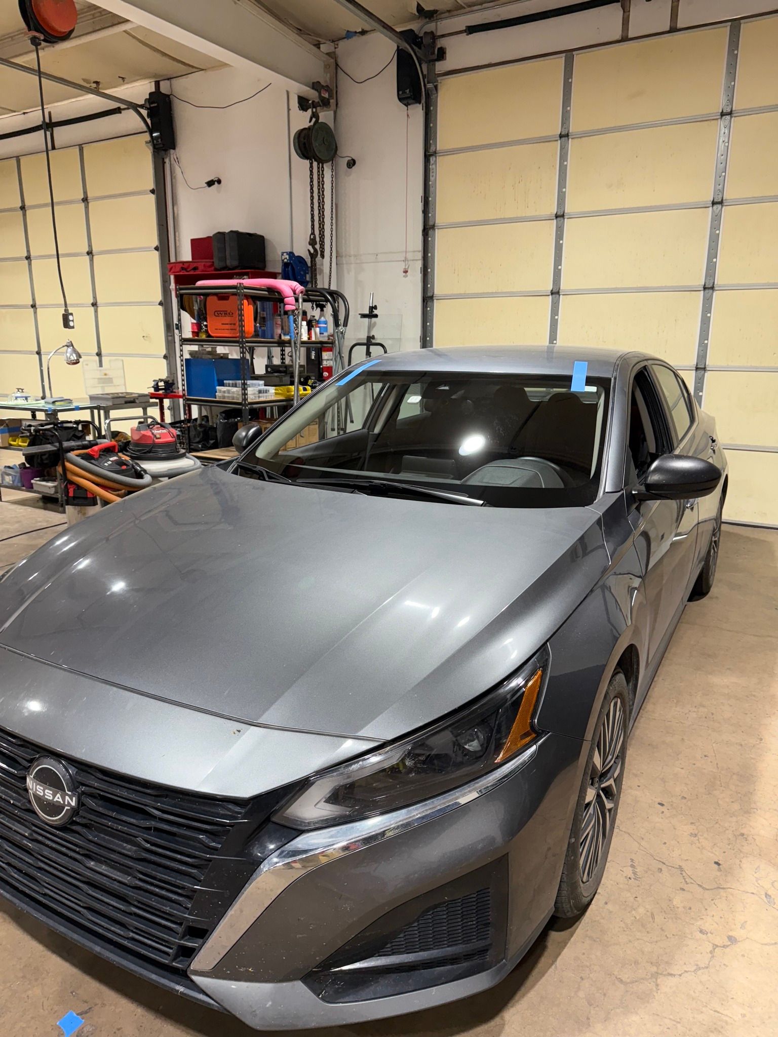 Gray Nissan Altima sedan inside a garage with the garage door open.