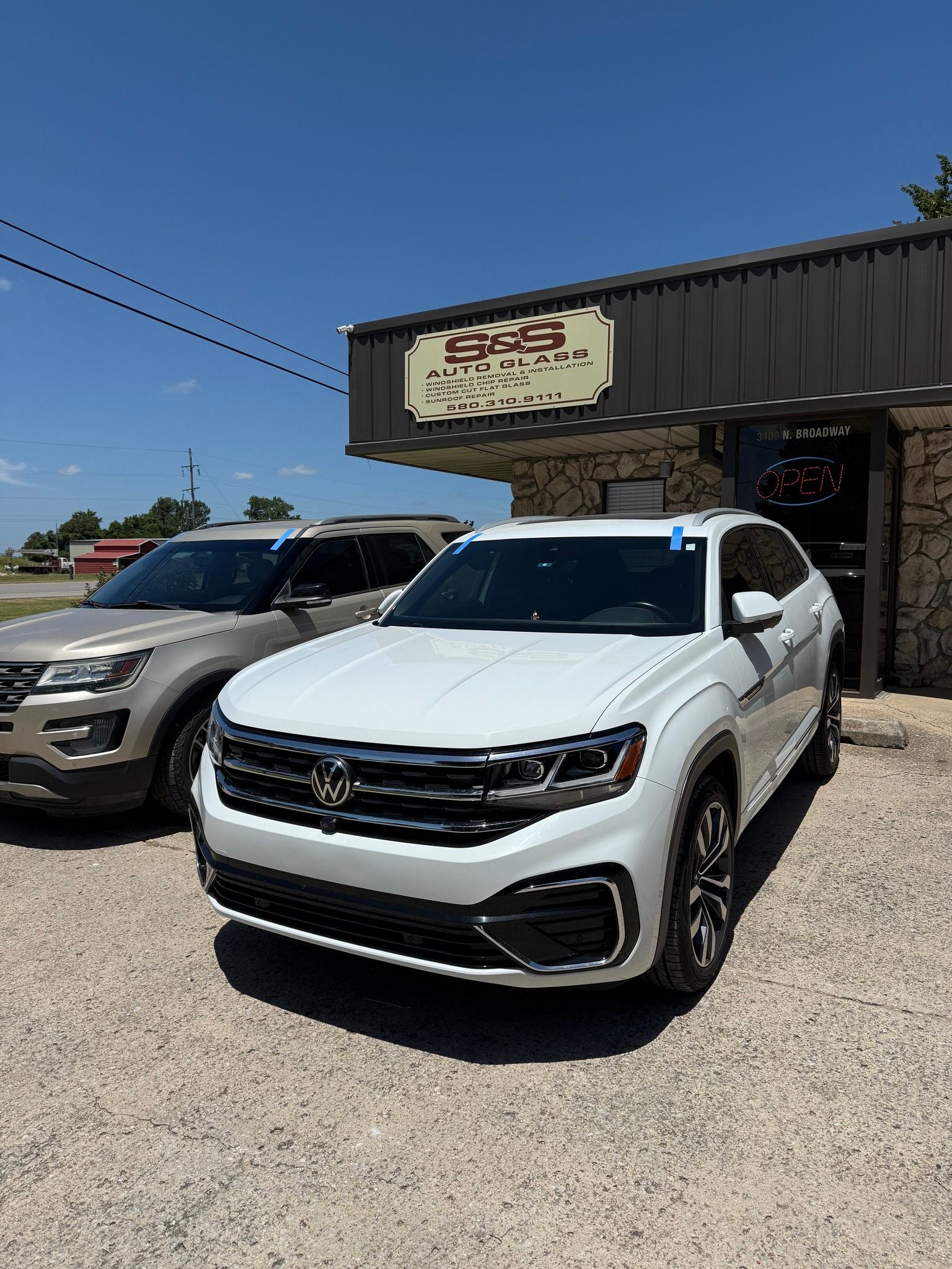 White Volkswagen Atlas parked in front of a building with a brown sign; a brown Ford Explorer is parked to the left.