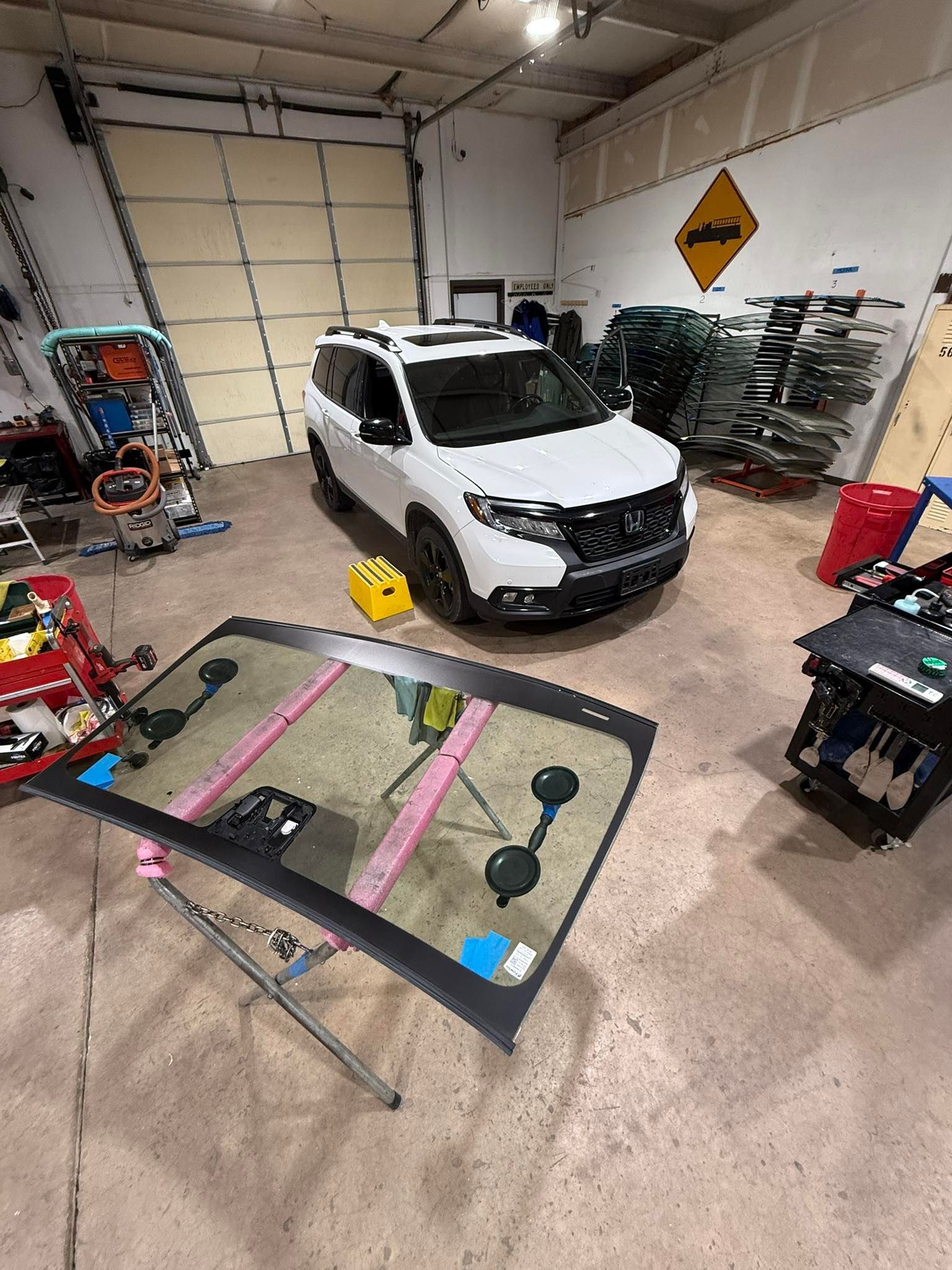 A white SUV in a shop with a windshield on a stand in front of it.