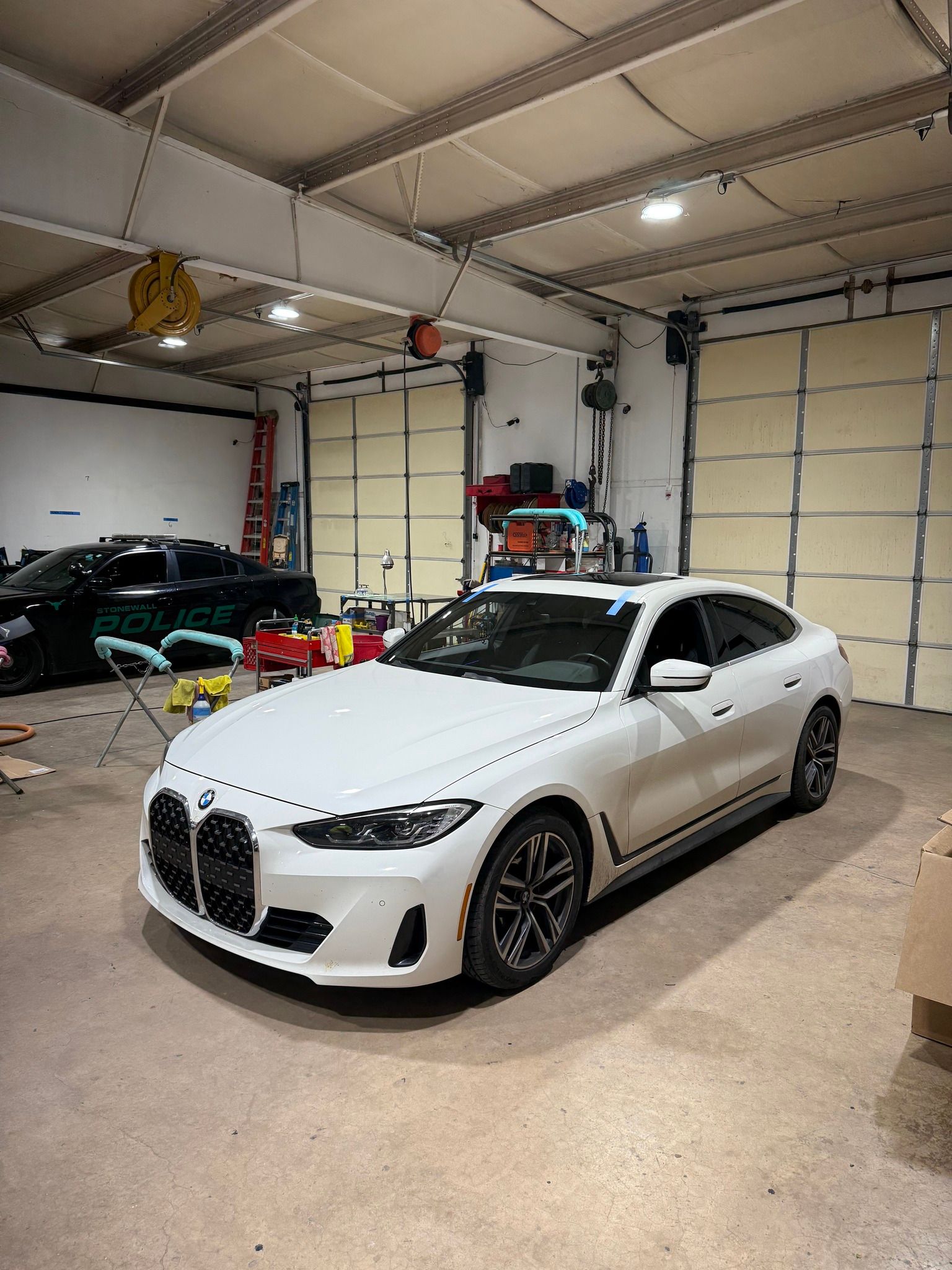 White BMW sedan in a garage, with a black car visible in the background.