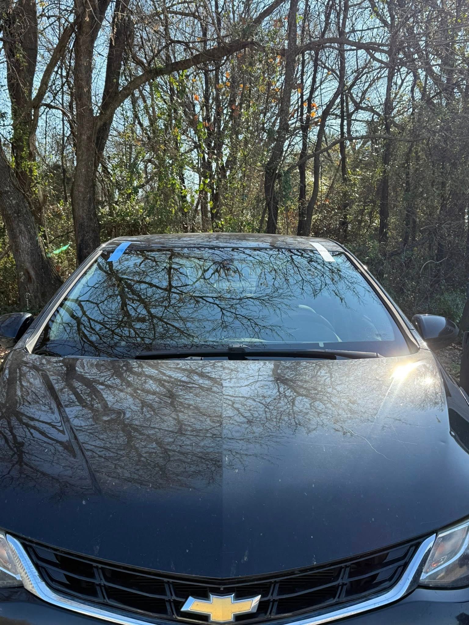 Black Chevrolet car with a reflective windshield, parked outdoors with a forest background.