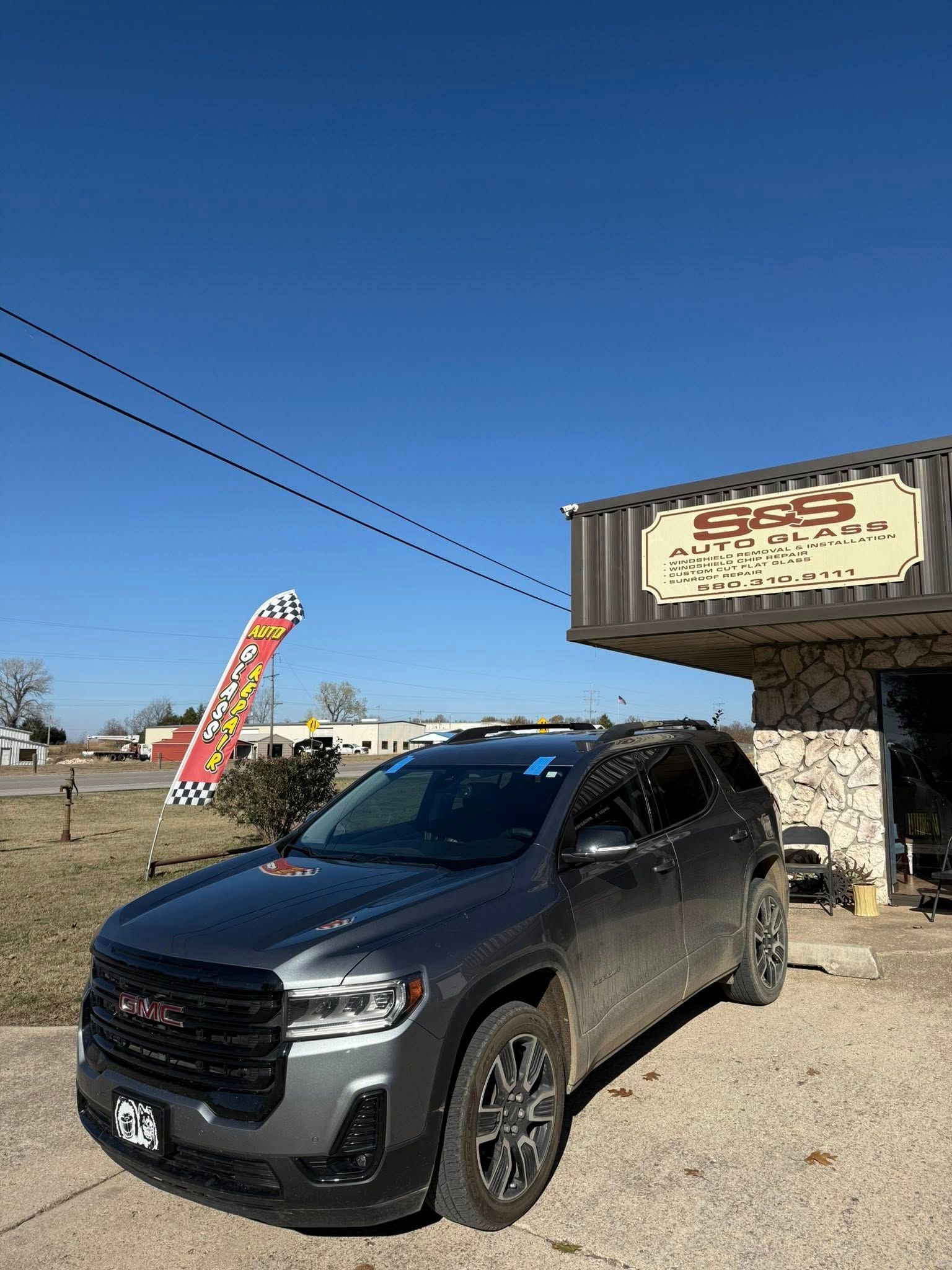 Dark gray GMC Acadia SUV parked outside a business with a sign. Blue sky overhead.