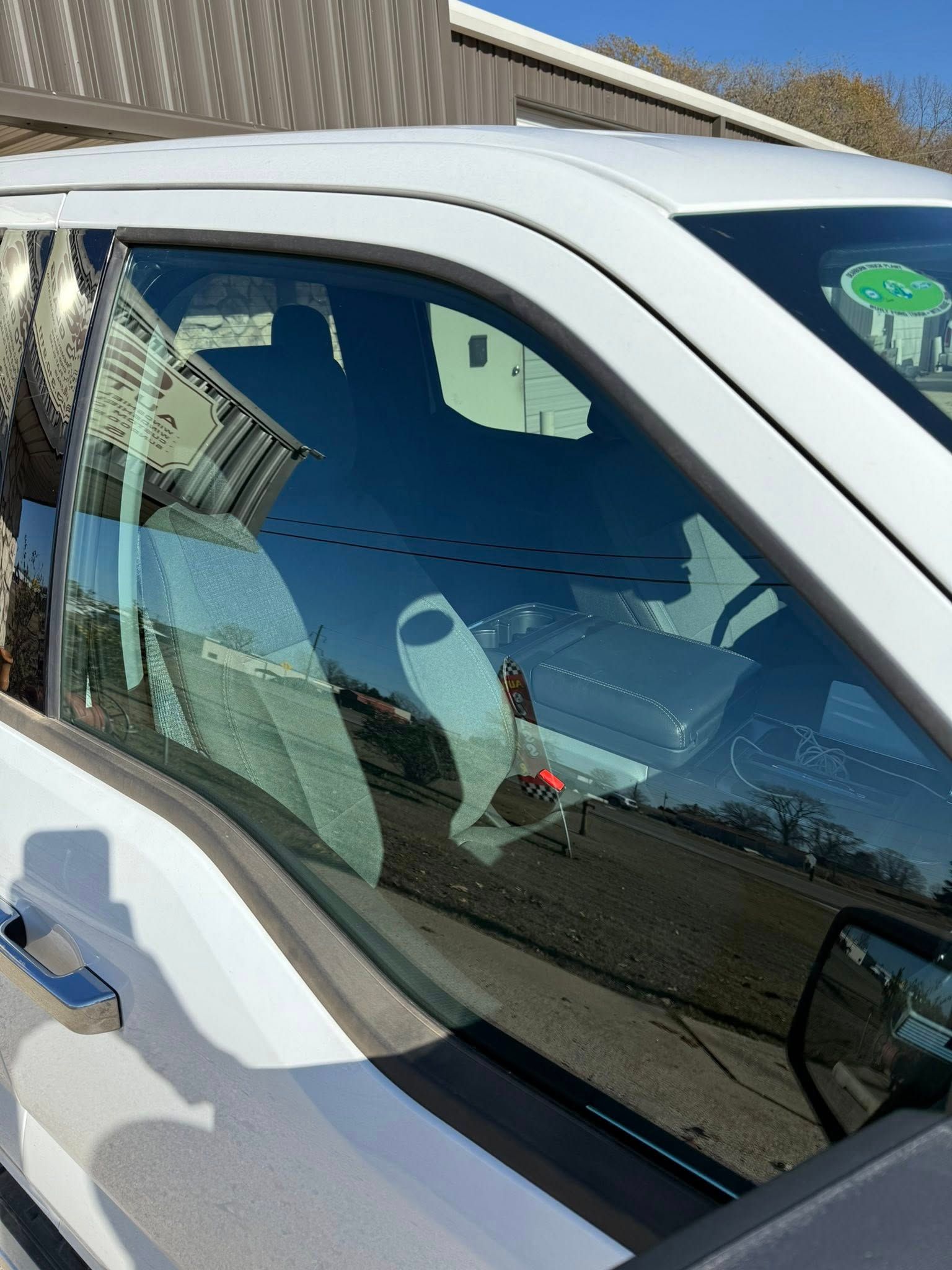 White truck's side window reflecting interior details, including a seat and objects, under a clear sky.
