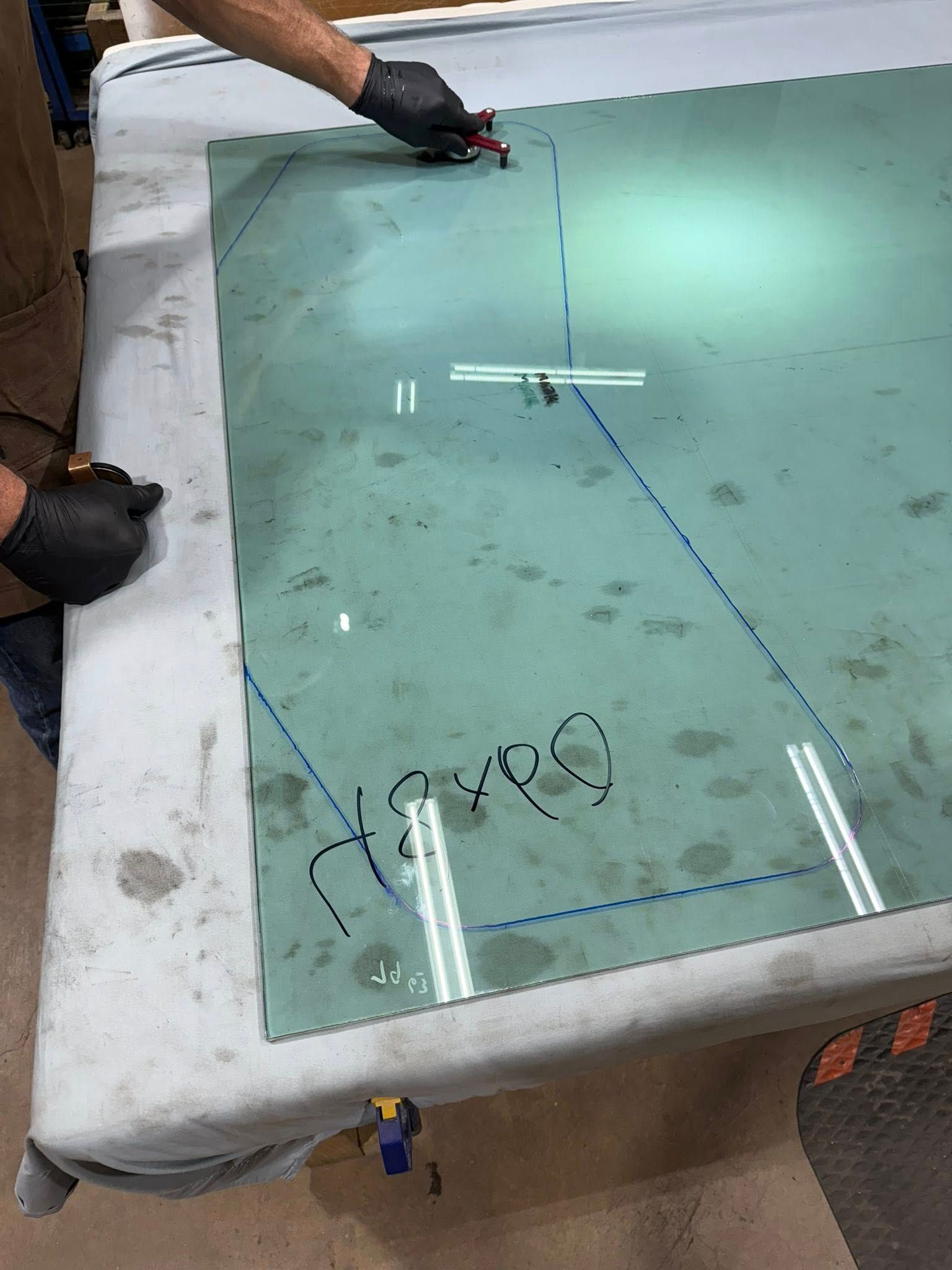 Person cutting glass with a tool, following a marked blue outline.