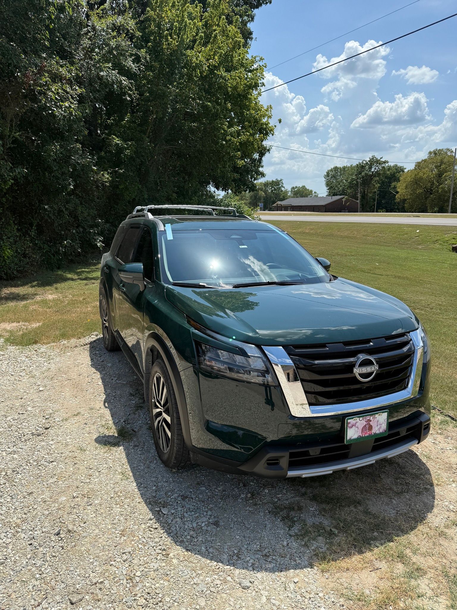 Dark green Nissan Pathfinder SUV parked on gravel driveway. Sunny day.