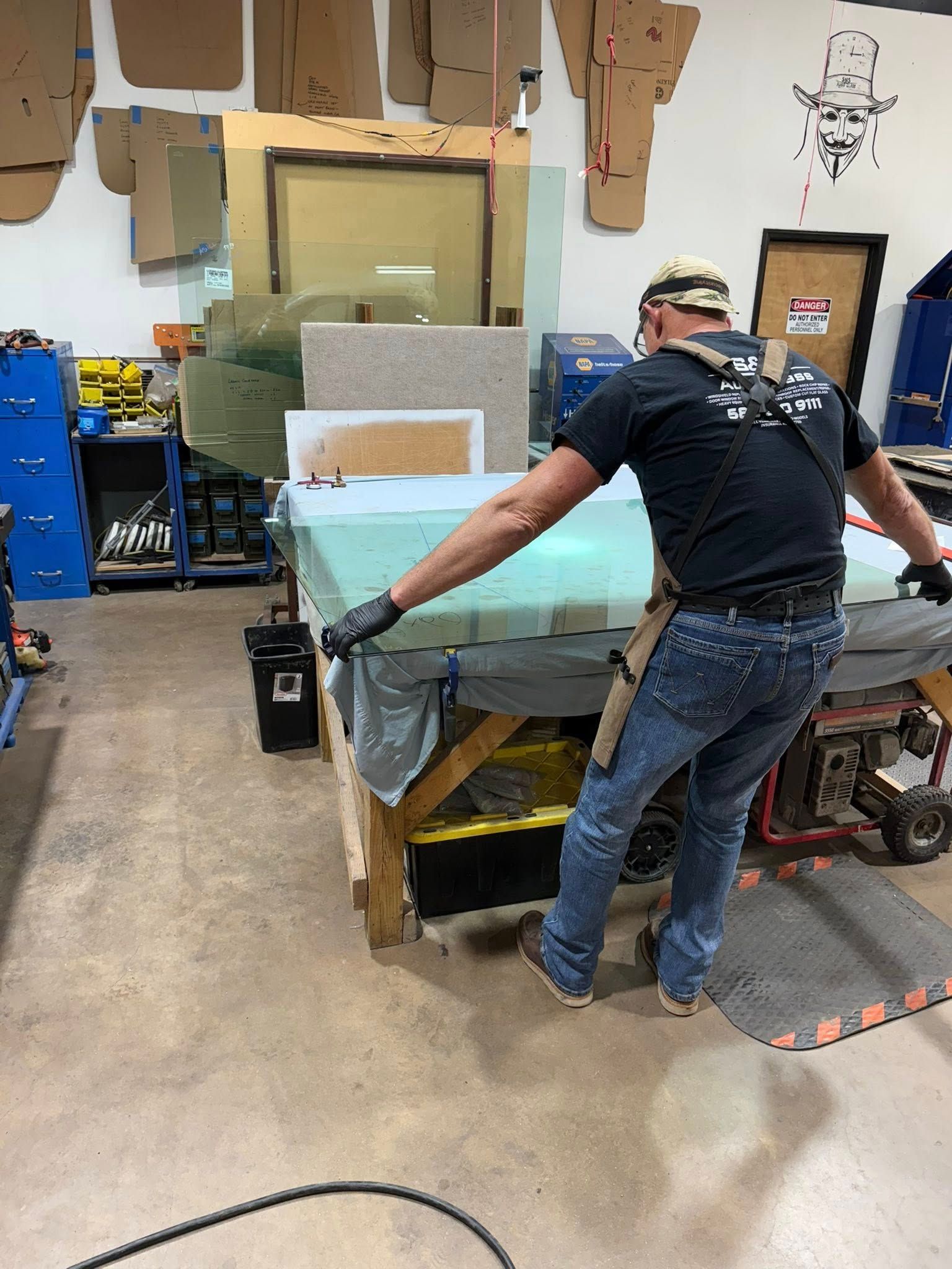Man in workshop, stretching a screen. He wears protective gear; workbench in focus.