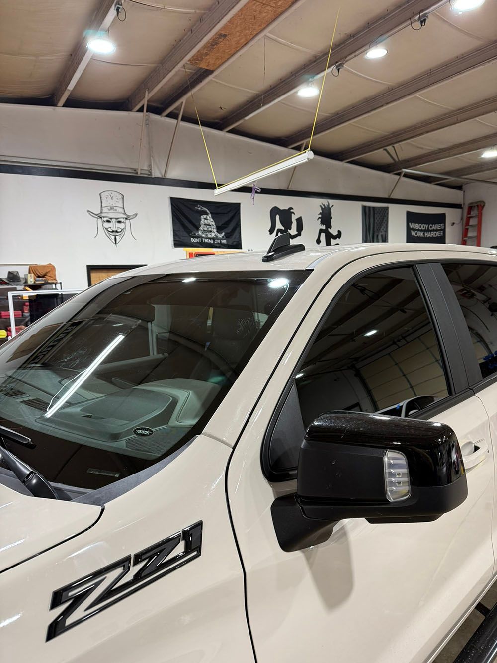 White pickup truck in a garage, showing the front side and black side mirror.