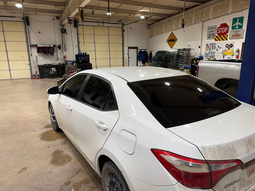 White sedan parked inside a garage with large closed doors and wall signs.