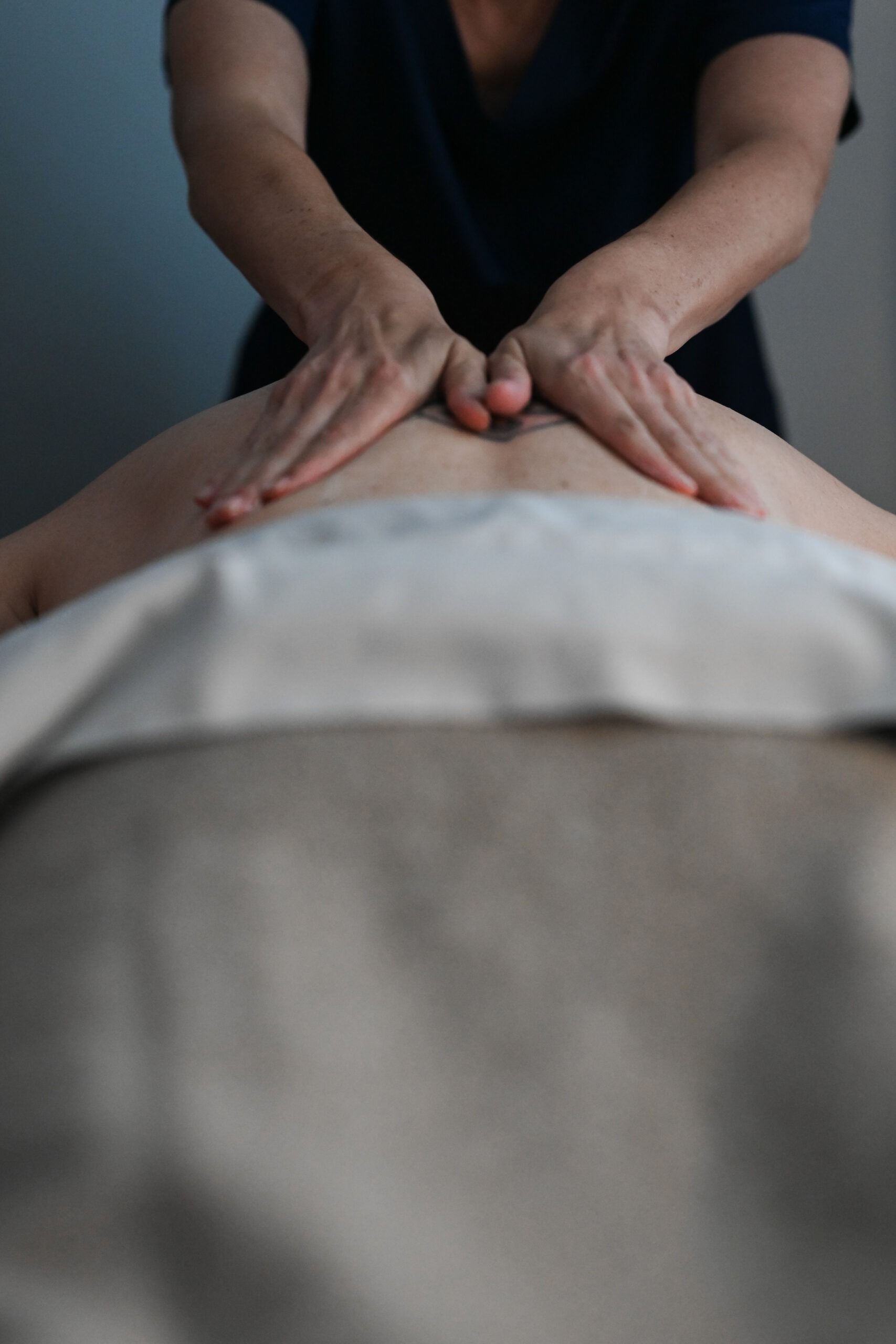 Hands giving a back massage. A person lies face down, covered by a tan sheet.