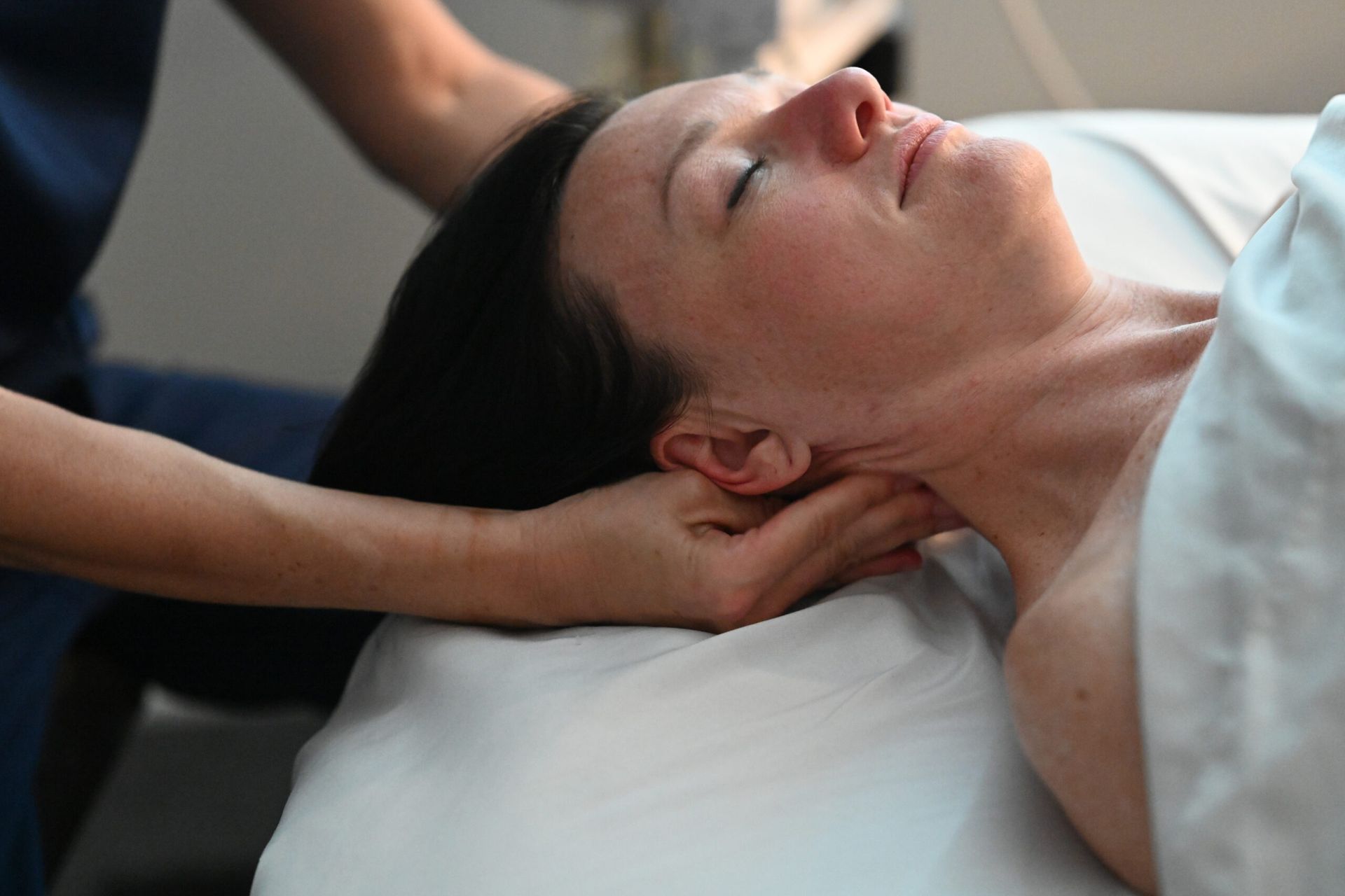 Person receiving neck massage on a massage table, eyes closed.