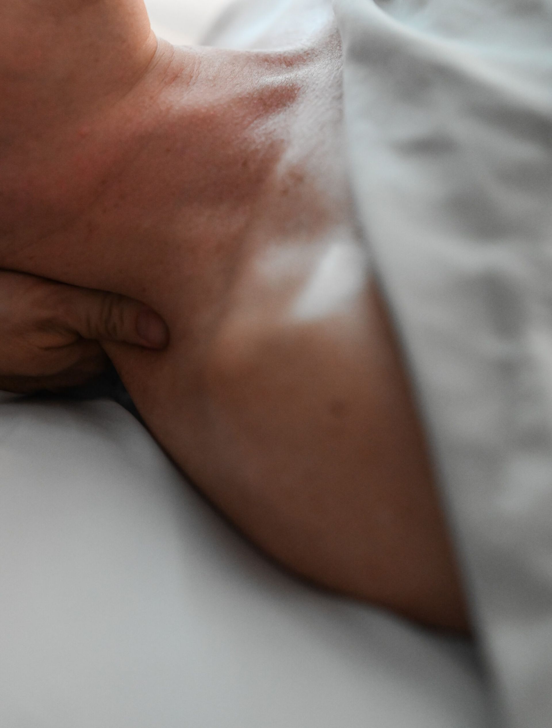 Person receiving neck and shoulder massage, close-up. Hand on neck, draped in white fabric.