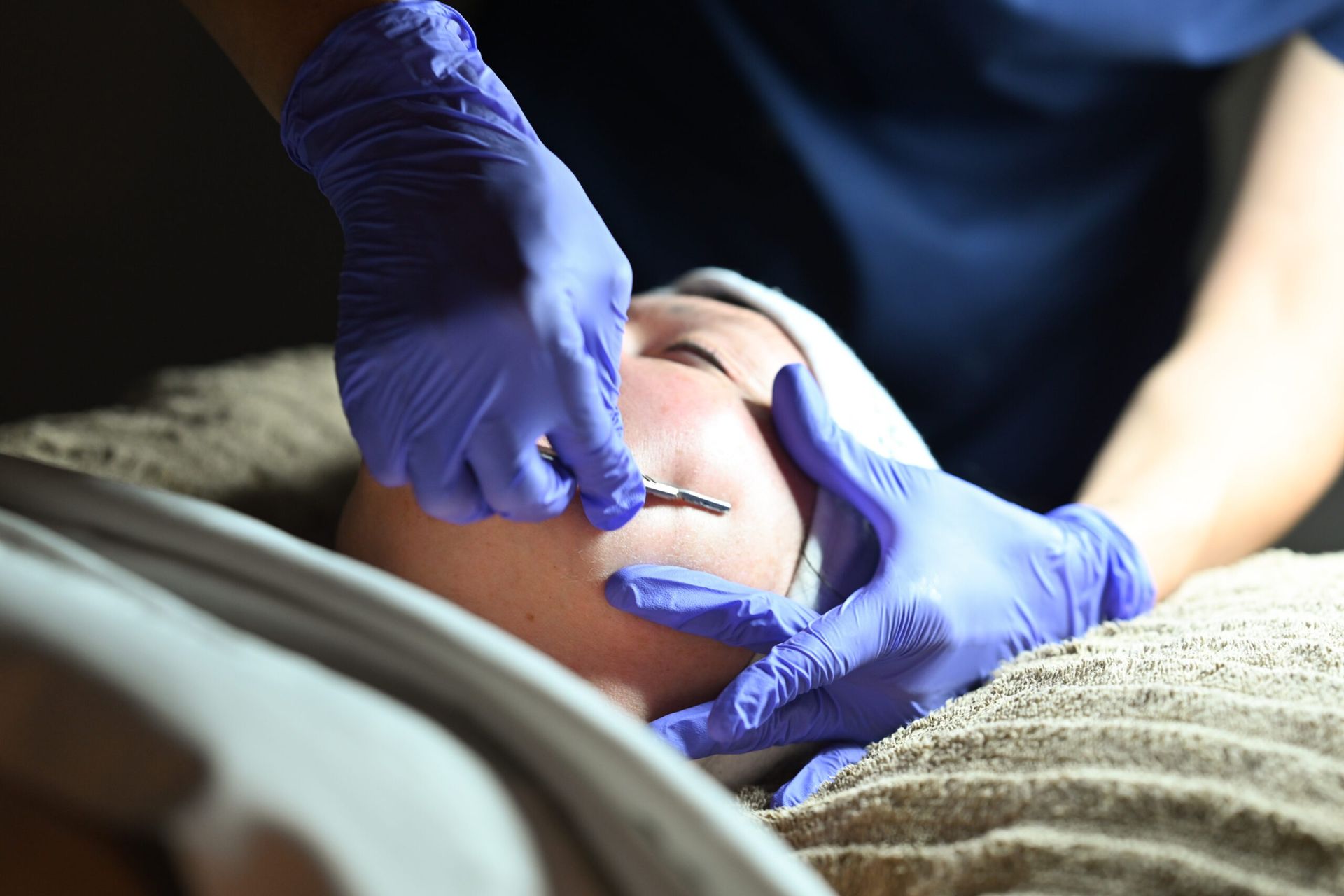 Facial treatment: A person's face being treated with a tool by gloved hands in a spa.