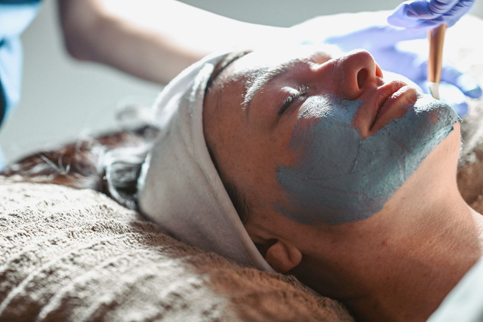 Woman with blue face mask at a spa, being treated by a professional.