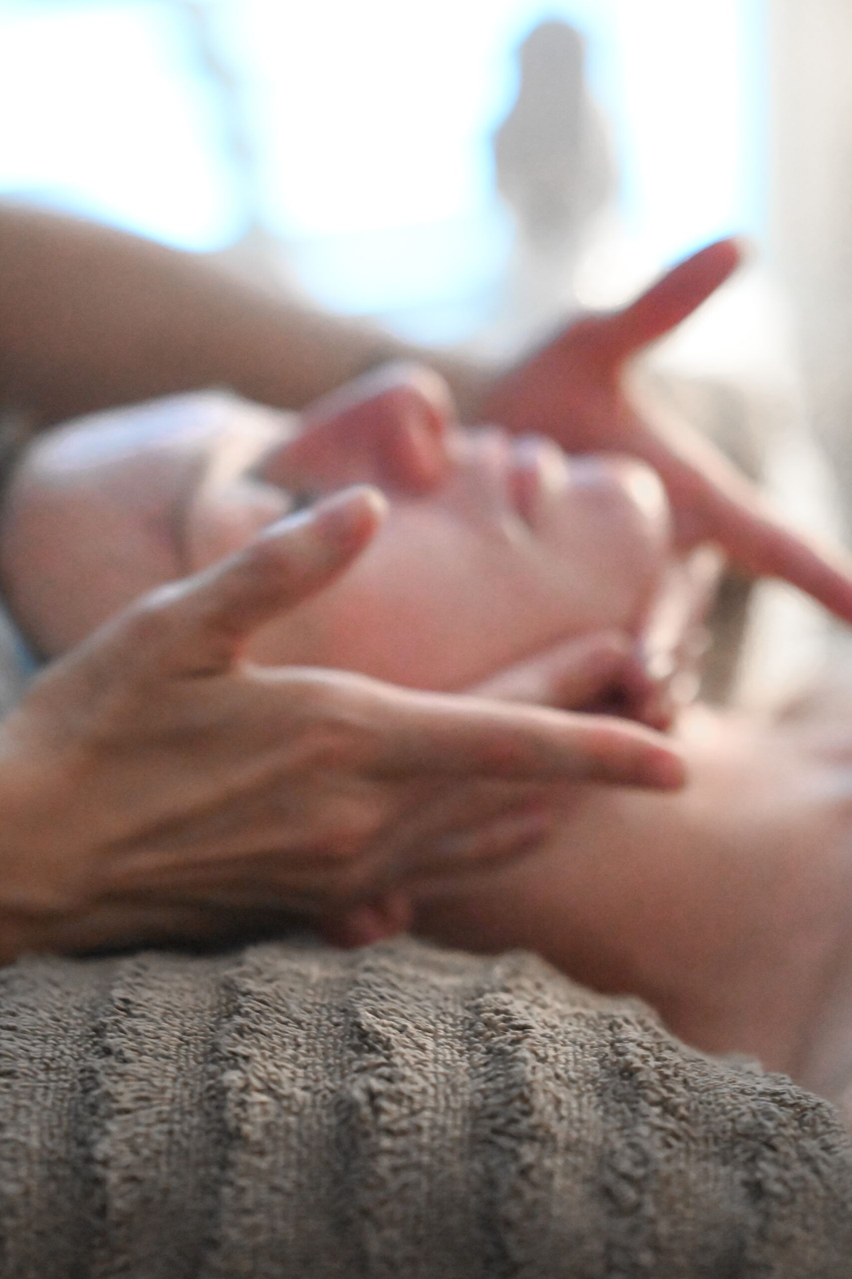 Hands gently cradling a person's face, possibly during a massage, with a soft focus and neutral tones.
