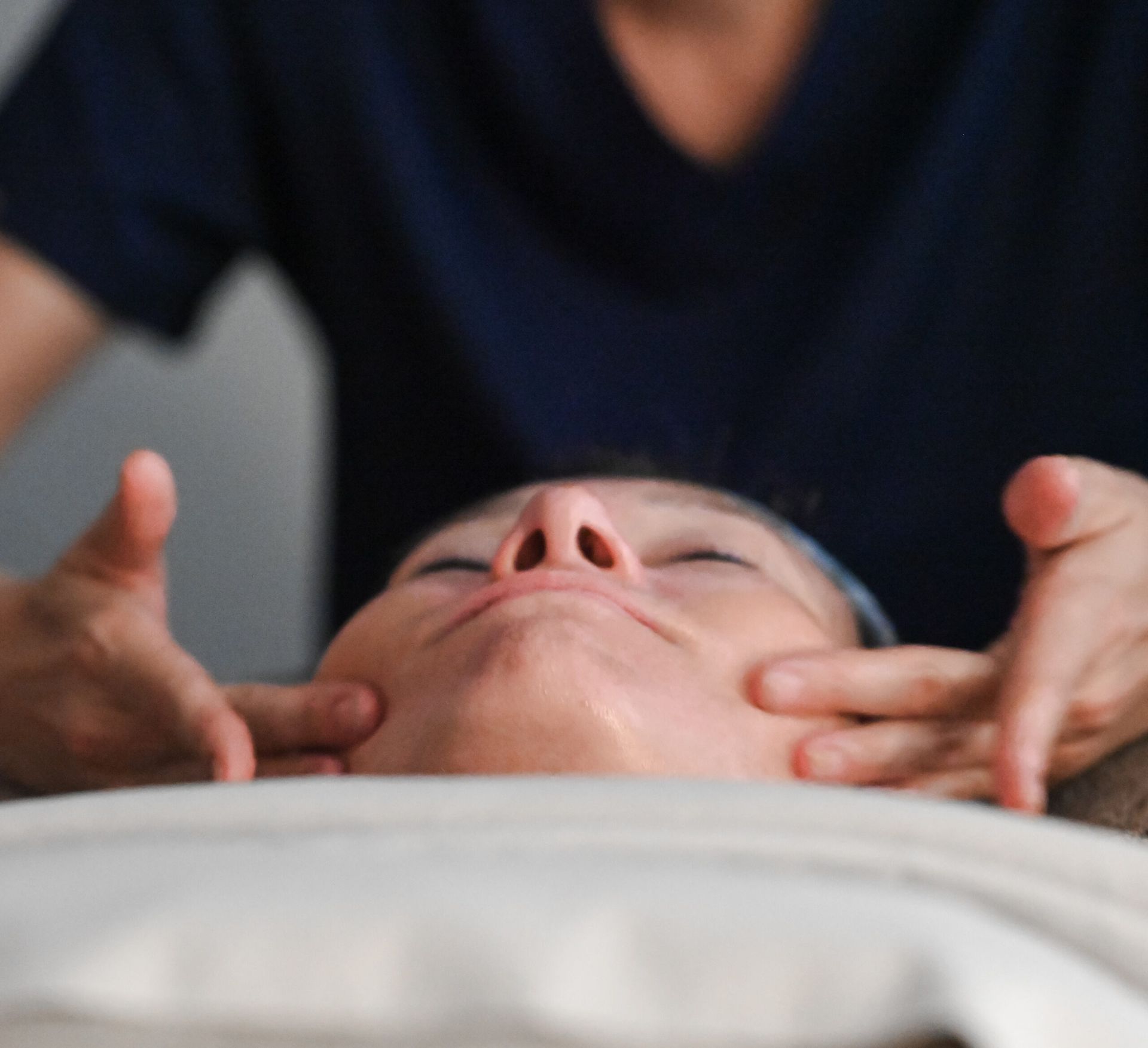 Woman receiving facial massage, hands on her cheeks. Eyes closed, neutral expression.