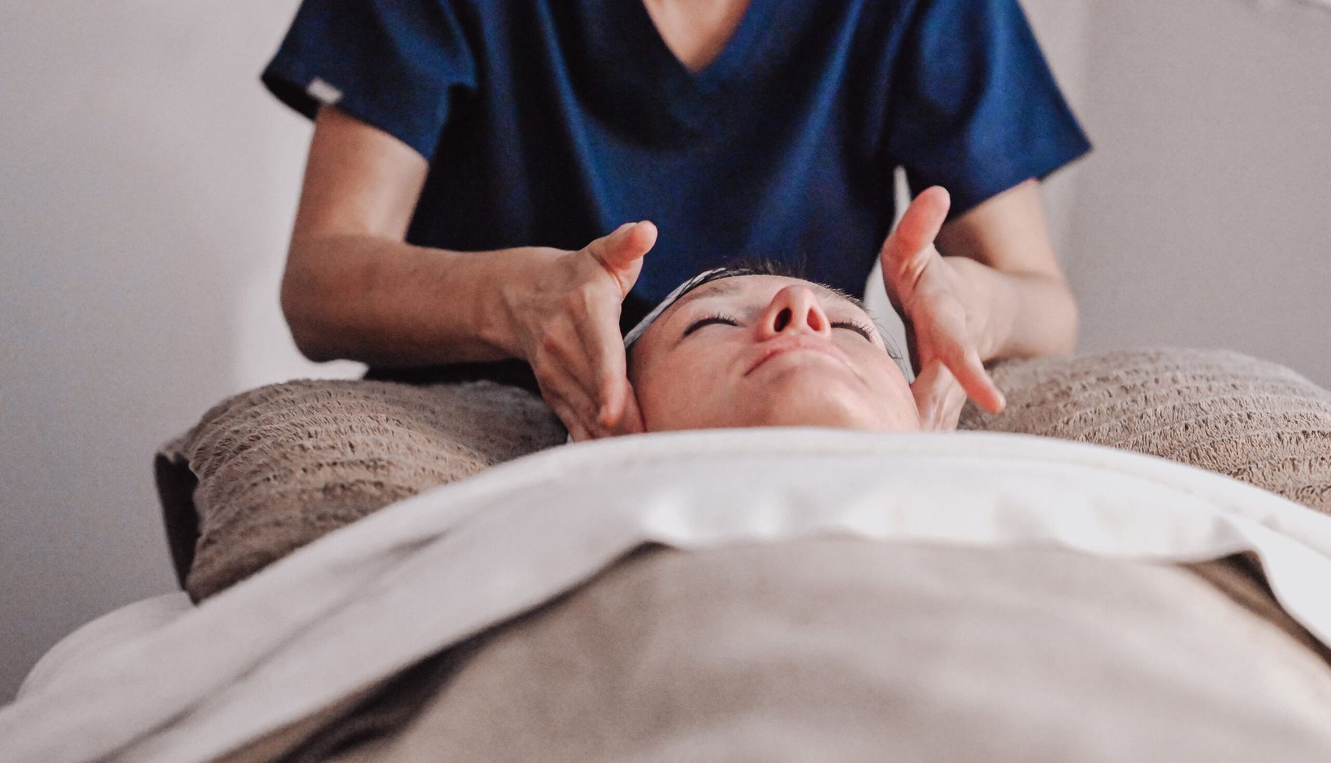 Woman receiving facial massage in a spa; hands gently caressing the face.