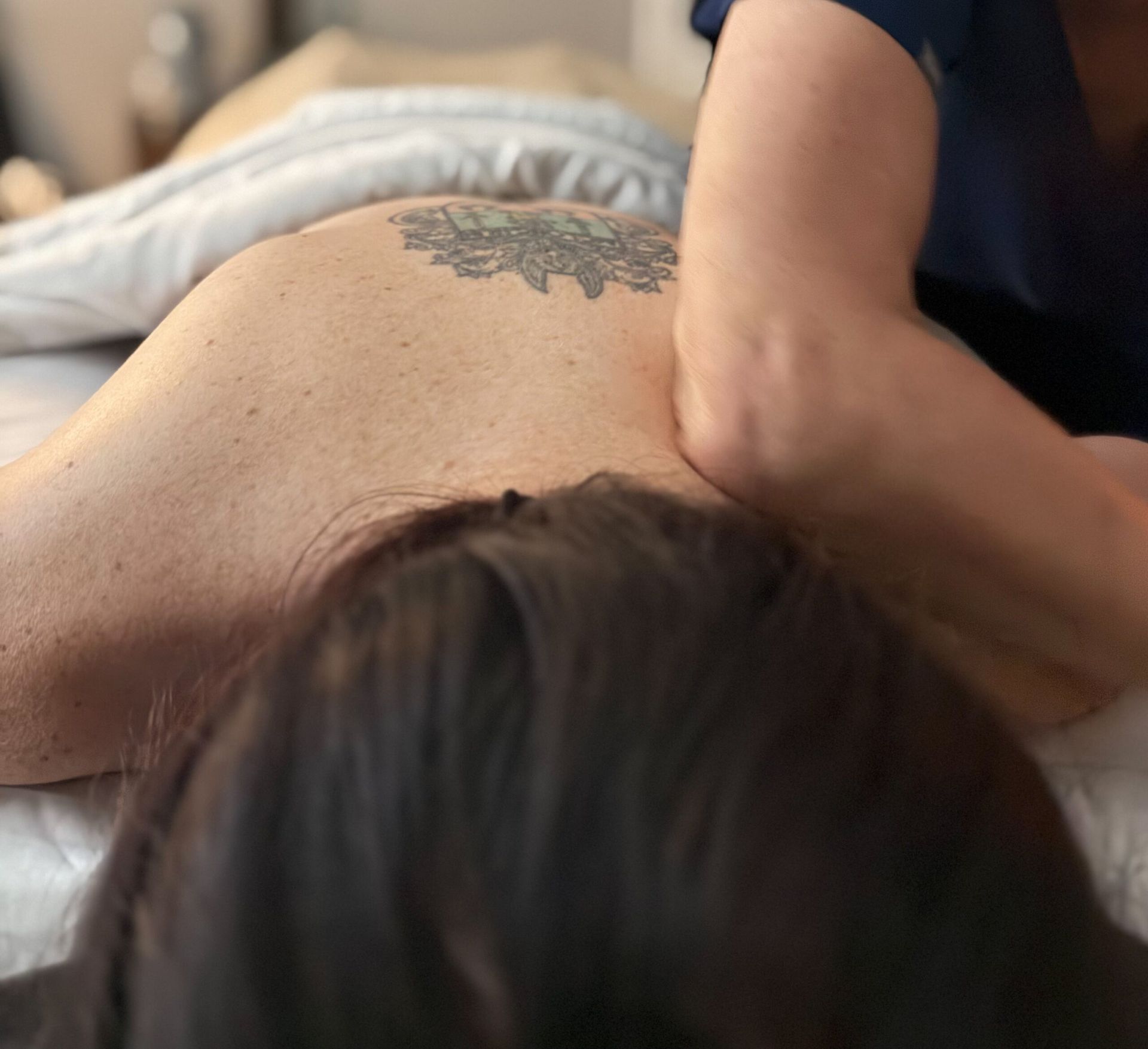 Person receiving a massage on their back; masseuse's arm is on the back.