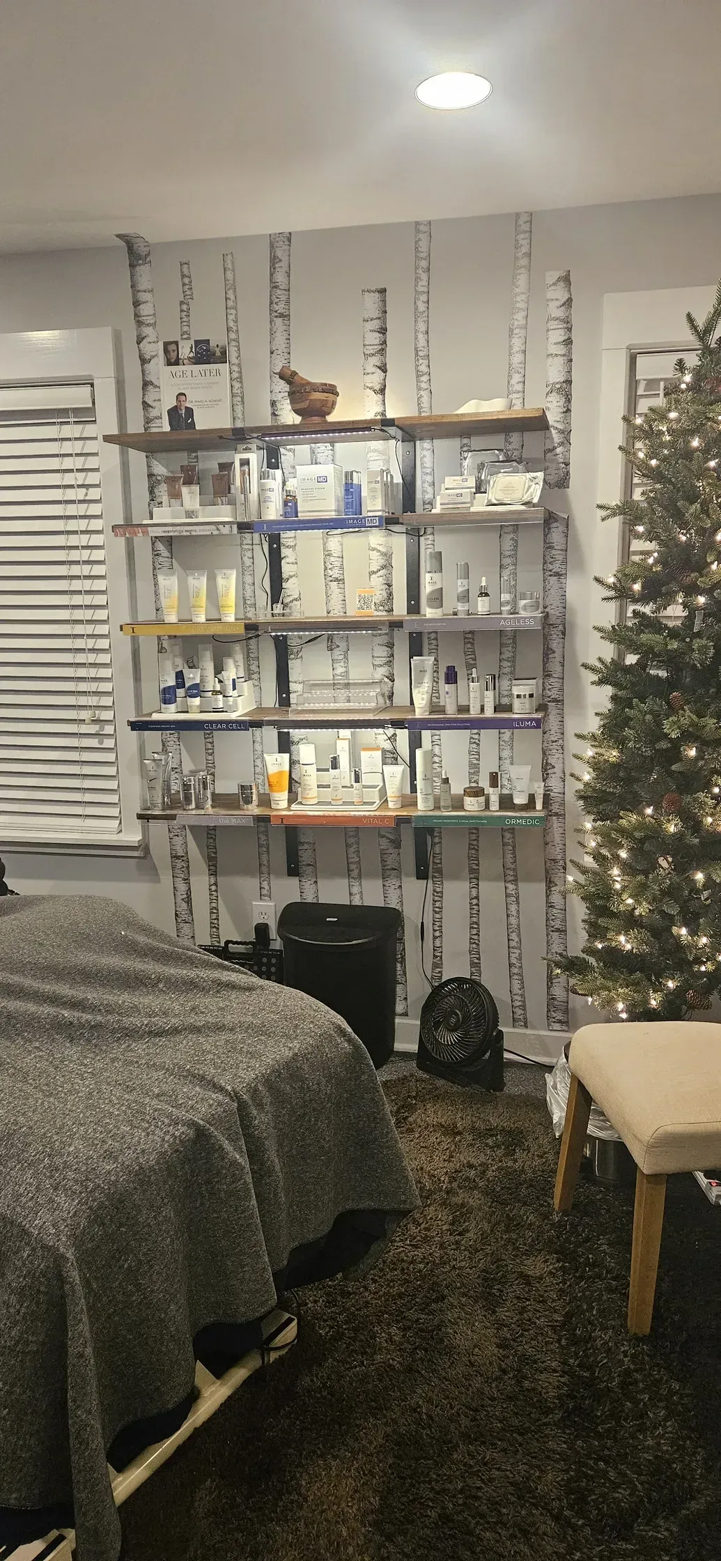 Bedroom with shelves, bed, Christmas tree, and chair. Shelves hold products against a birch-look wall.