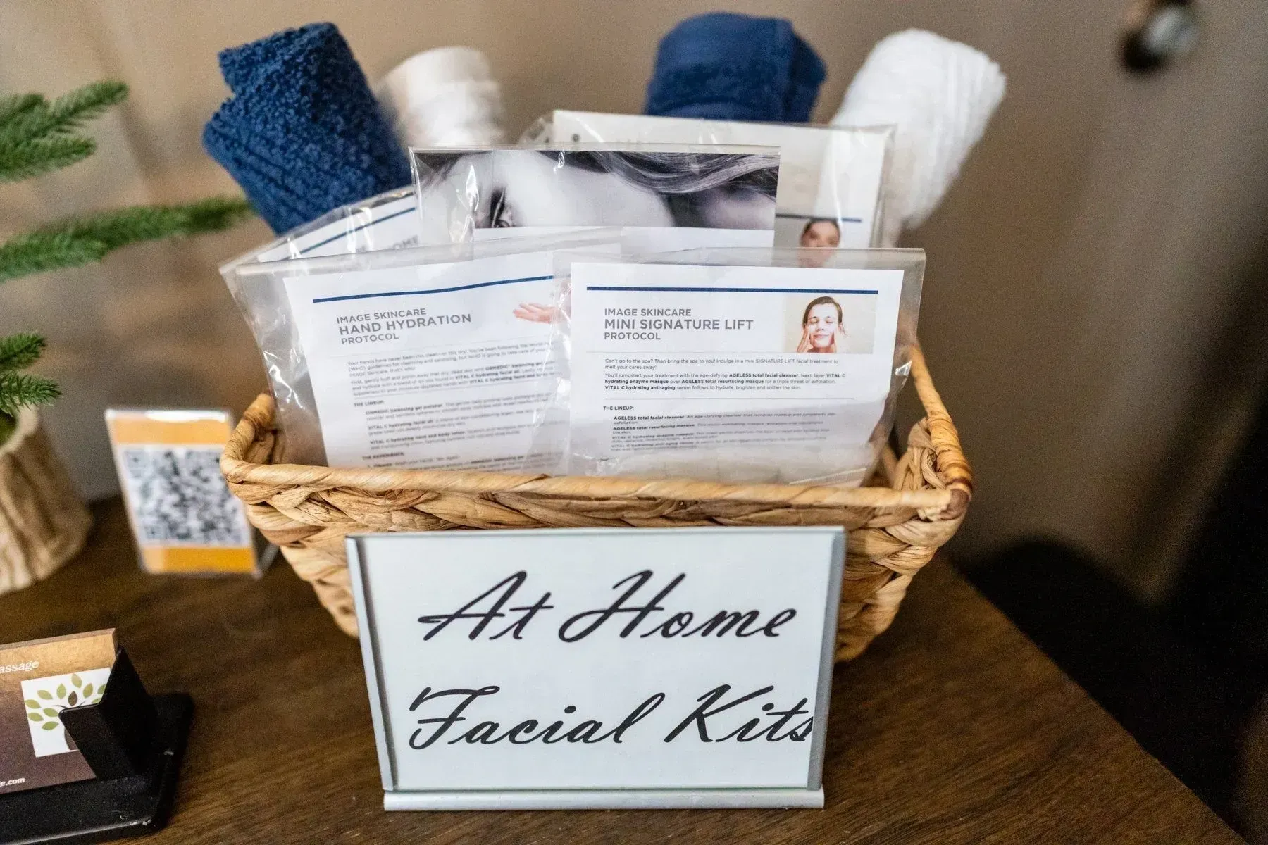 A basket of at-home facial kits, including towels, packaged products, and a sign.