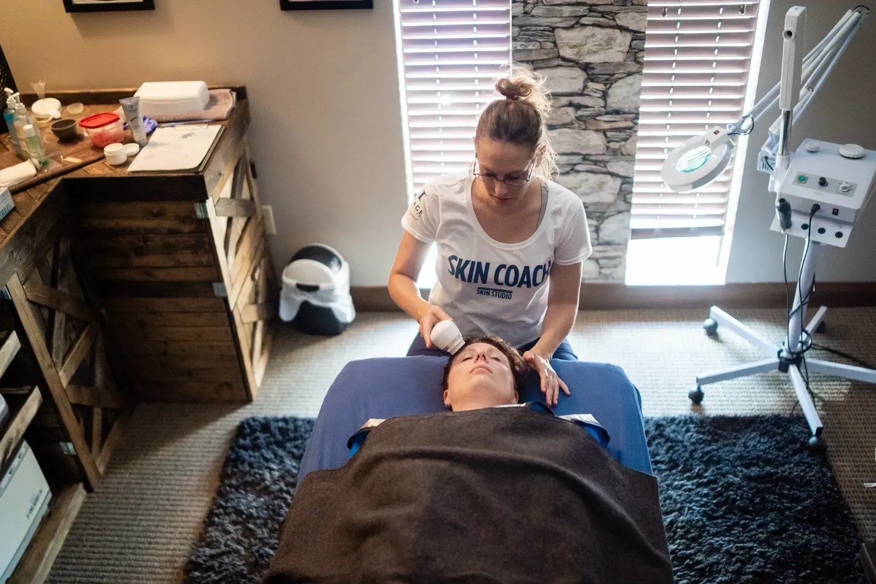 Woman giving facial treatment to a client lying on a massage bed.