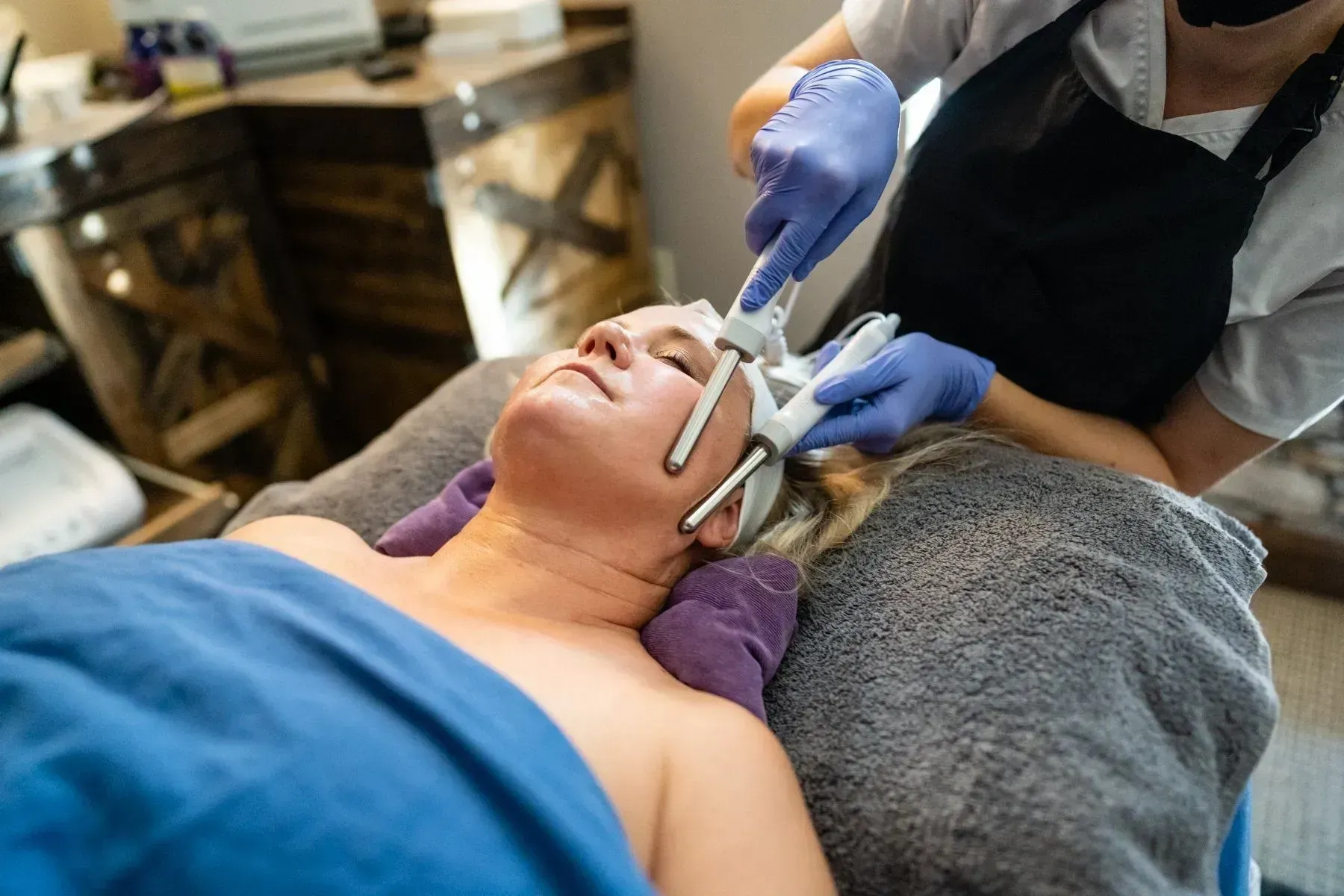 Woman receiving a facial treatment at a spa. Therapist using handheld device on her face, wearing gloves.