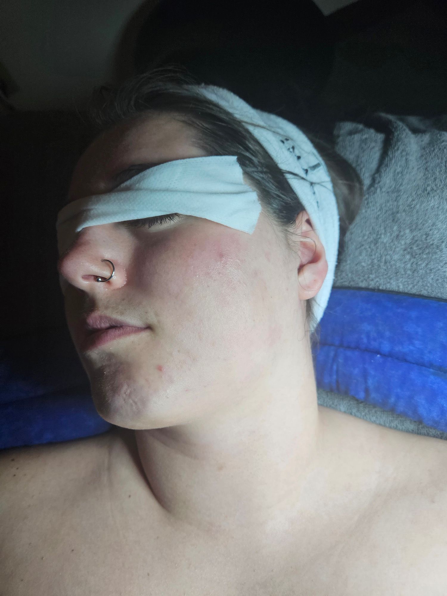 Person with a nose ring and blindfold lying down, likely at a spa.