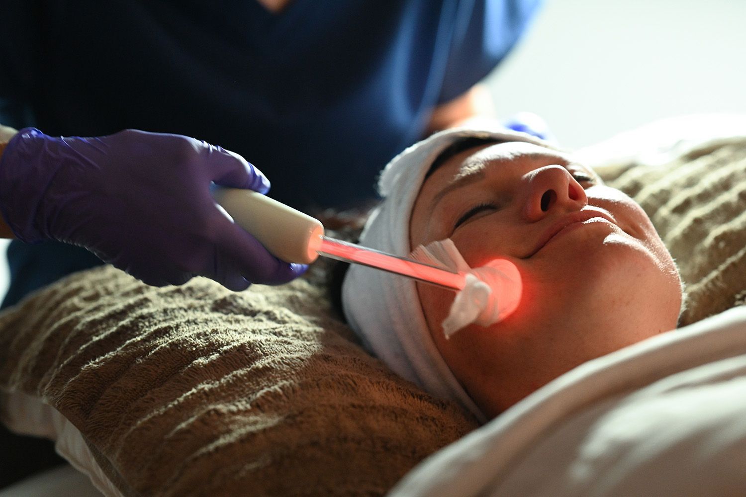 Woman receiving facial treatment with a glowing wand, eyes closed.