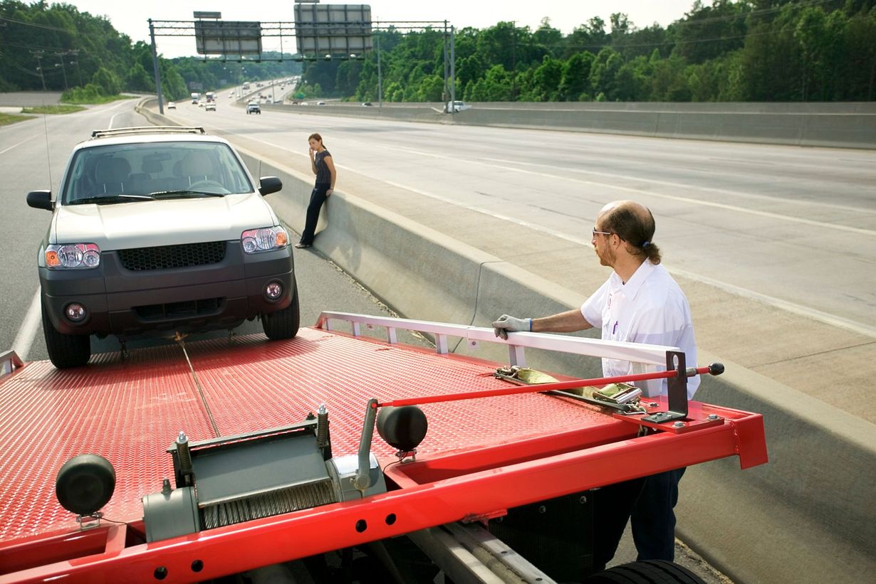 Tow truck loading a black SUV on a highway shoulder while a man stands nearby