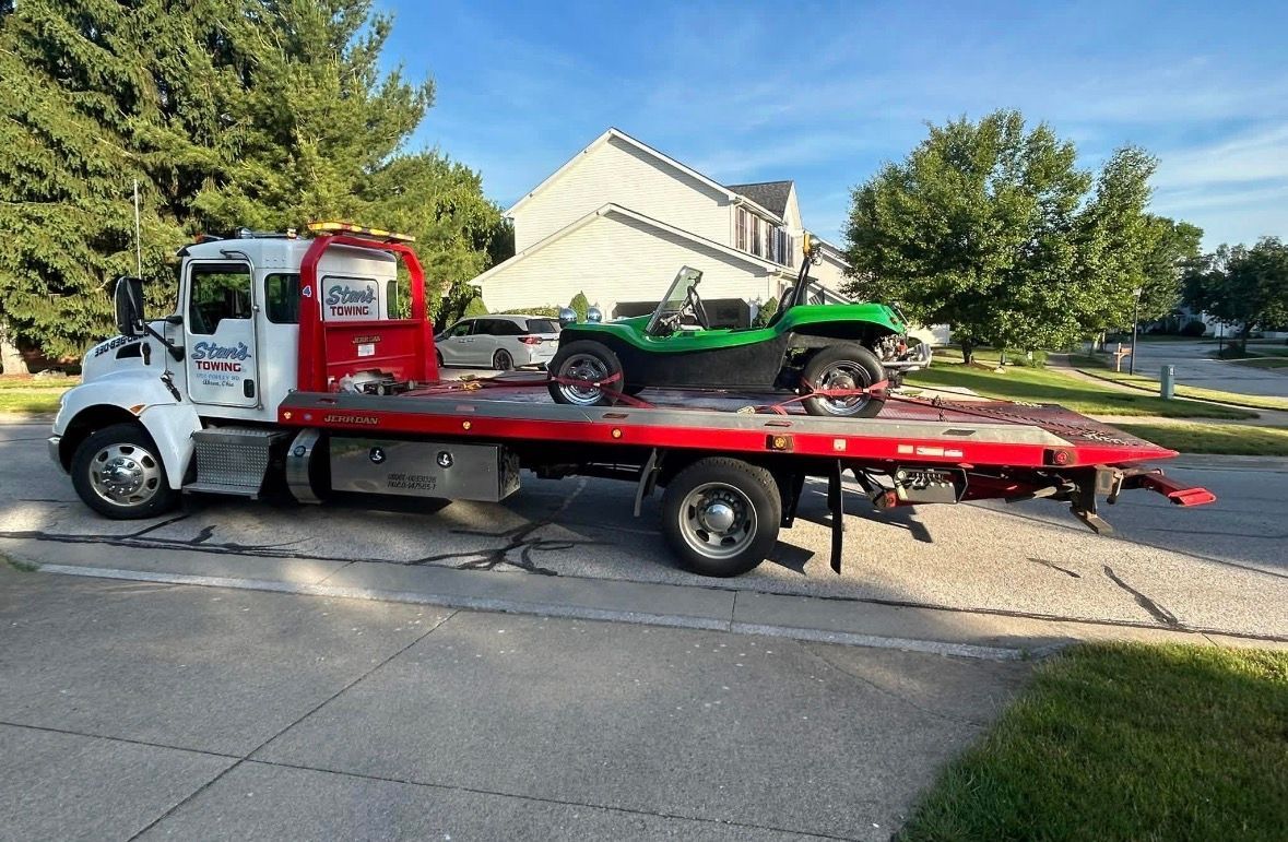 Tow truck hauling a red flatbed trailer with a green ATV on a suburban street