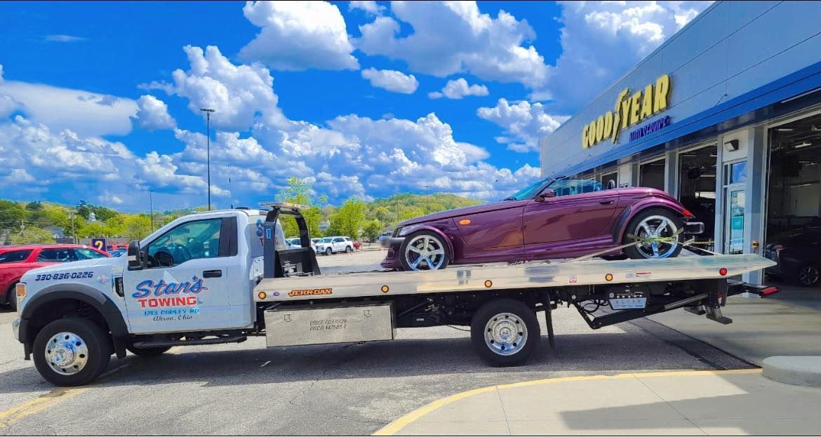 Tow truck carrying a maroon car outside a dealership on a sunny day