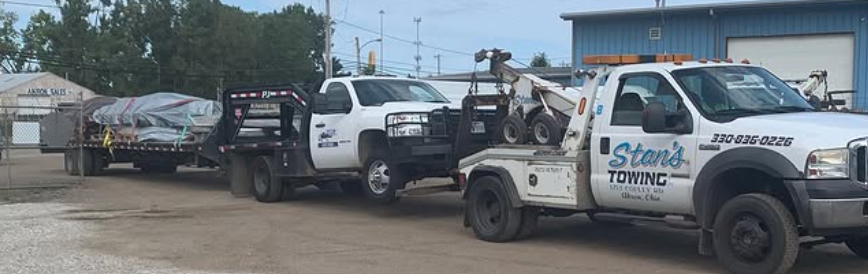 Two white tow trucks loaded with vehicles parked in a lot under a cloudy sky